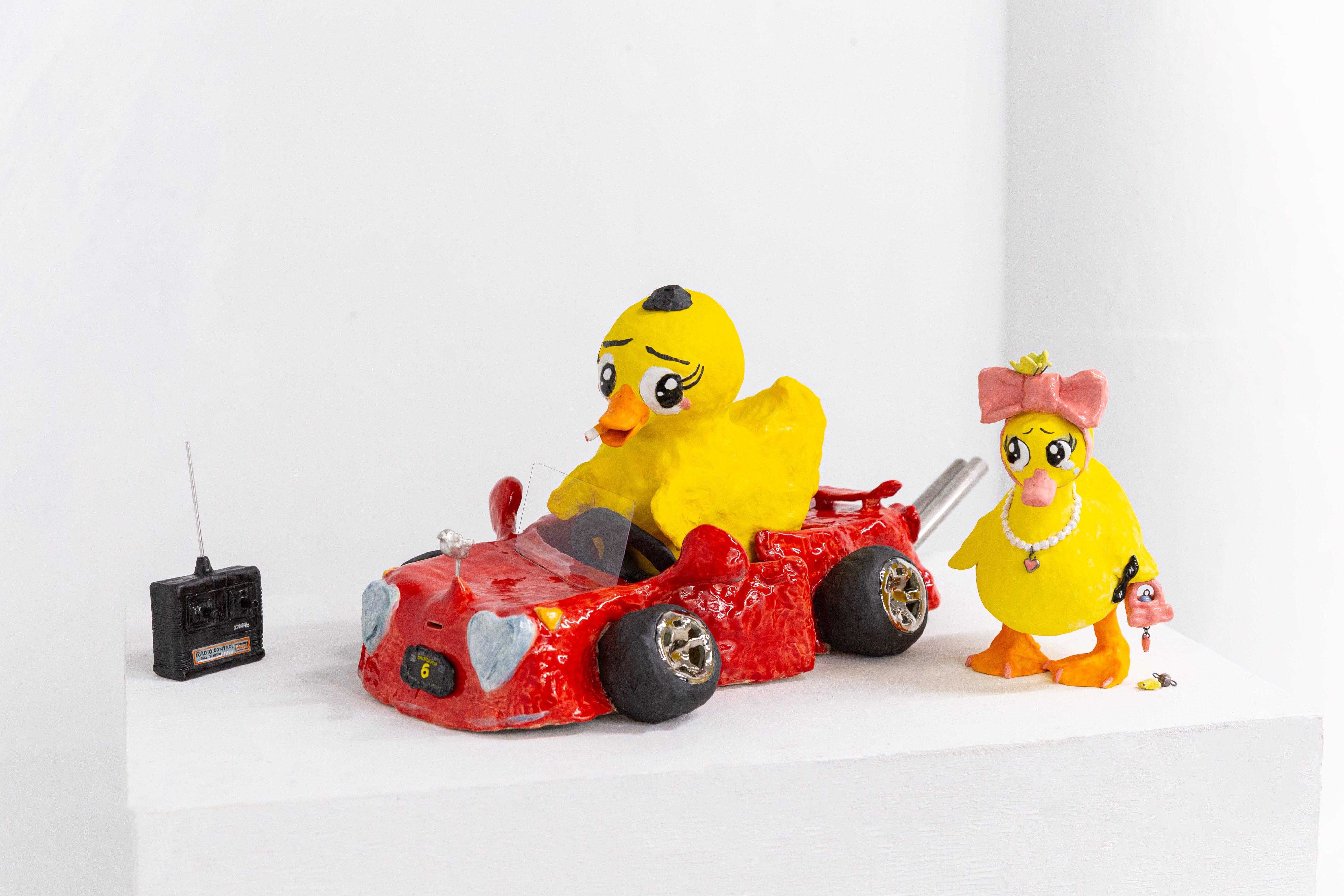 Ceramic sculpture of two ducks with human-like expressions in a red car. Glossy, playful yet uneasy, mixing childhood memory with subtle discomfort.