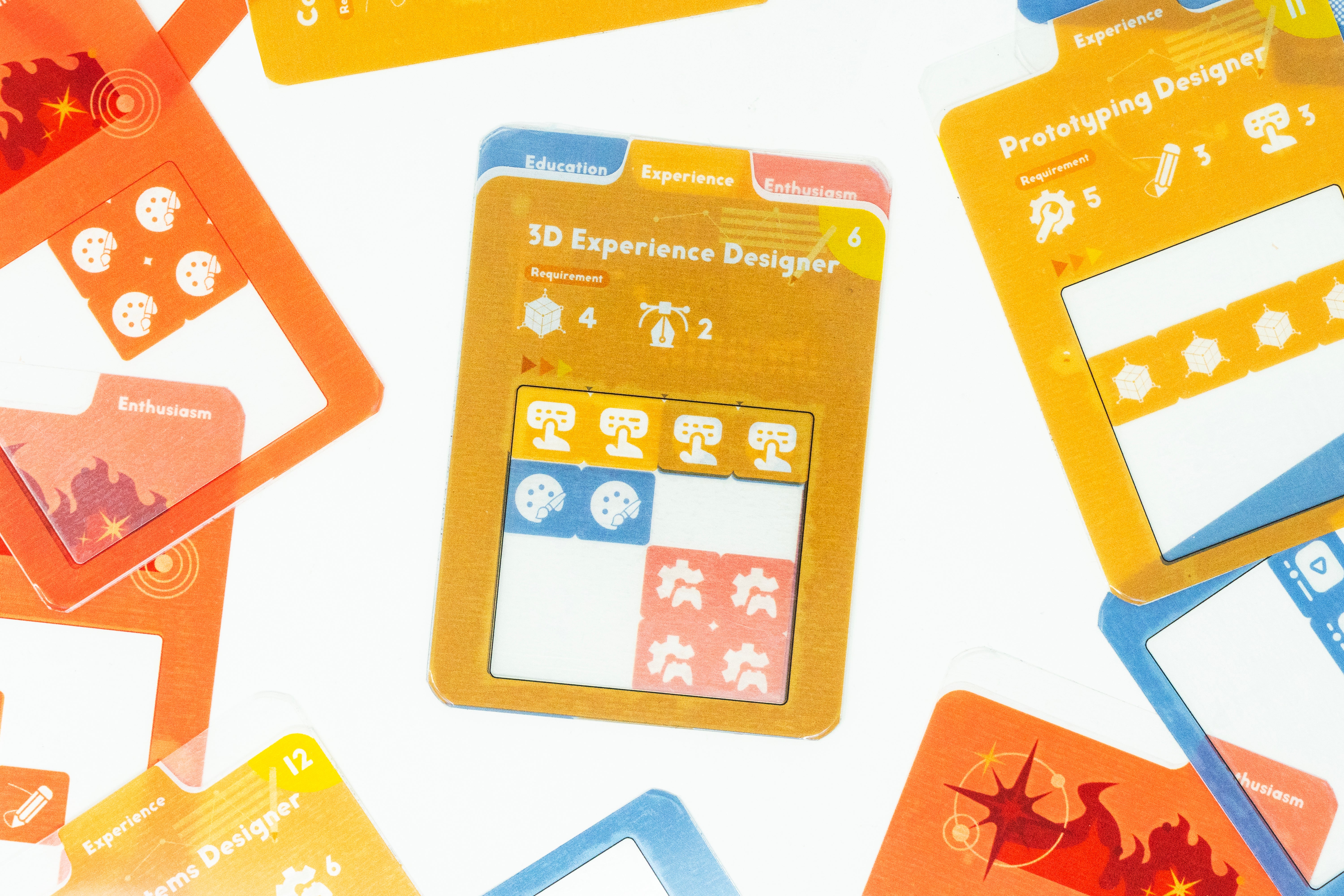 Colorful tabletop board game prototype showing transparent overlay cards, modular experience tiles, and job-description cards used for resume-building and persuasive communication role-play.