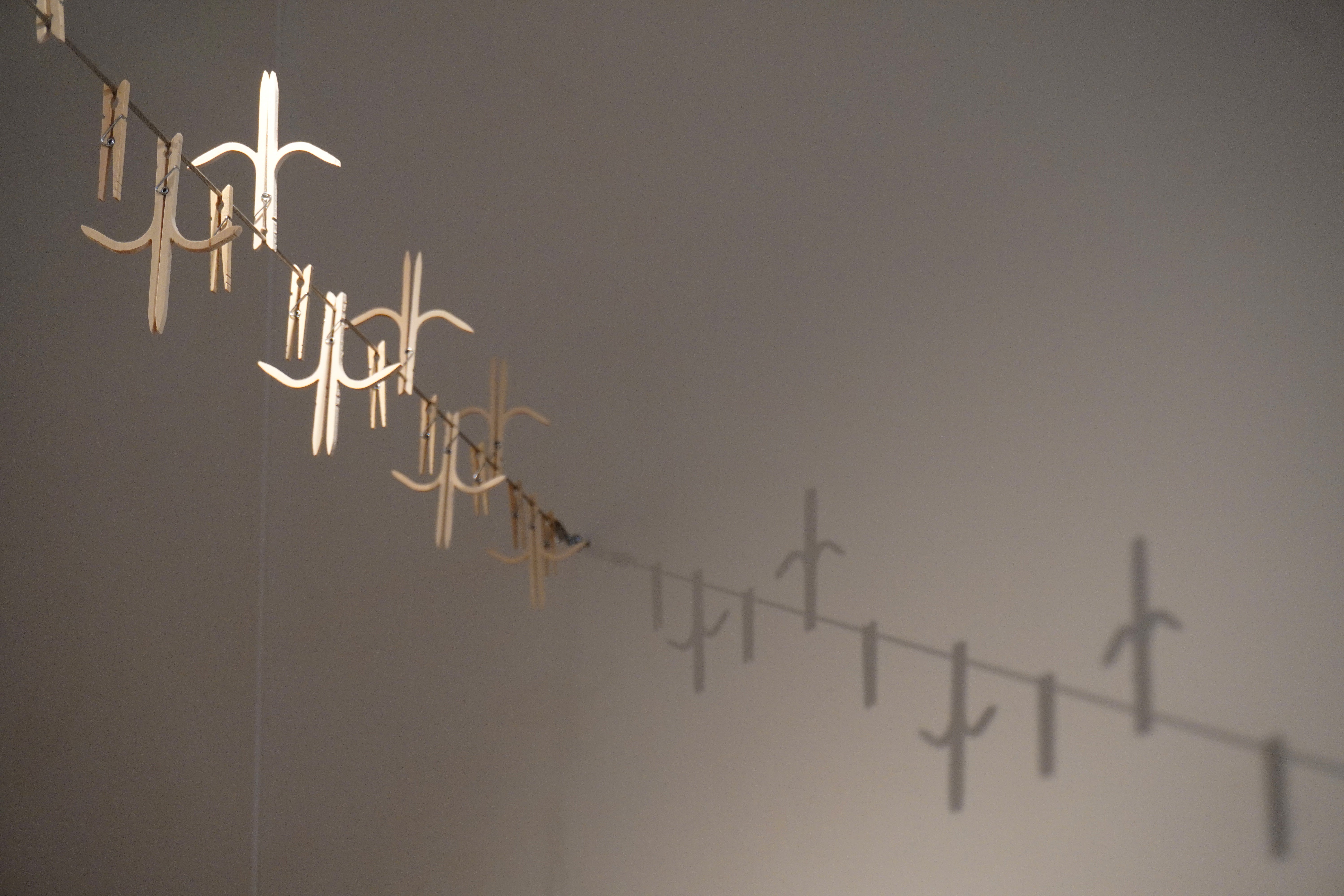Modified wooden clothespins on a steel clothesline that have a shape of an anticlimbing fence with spikes pointing upwards and downwards.