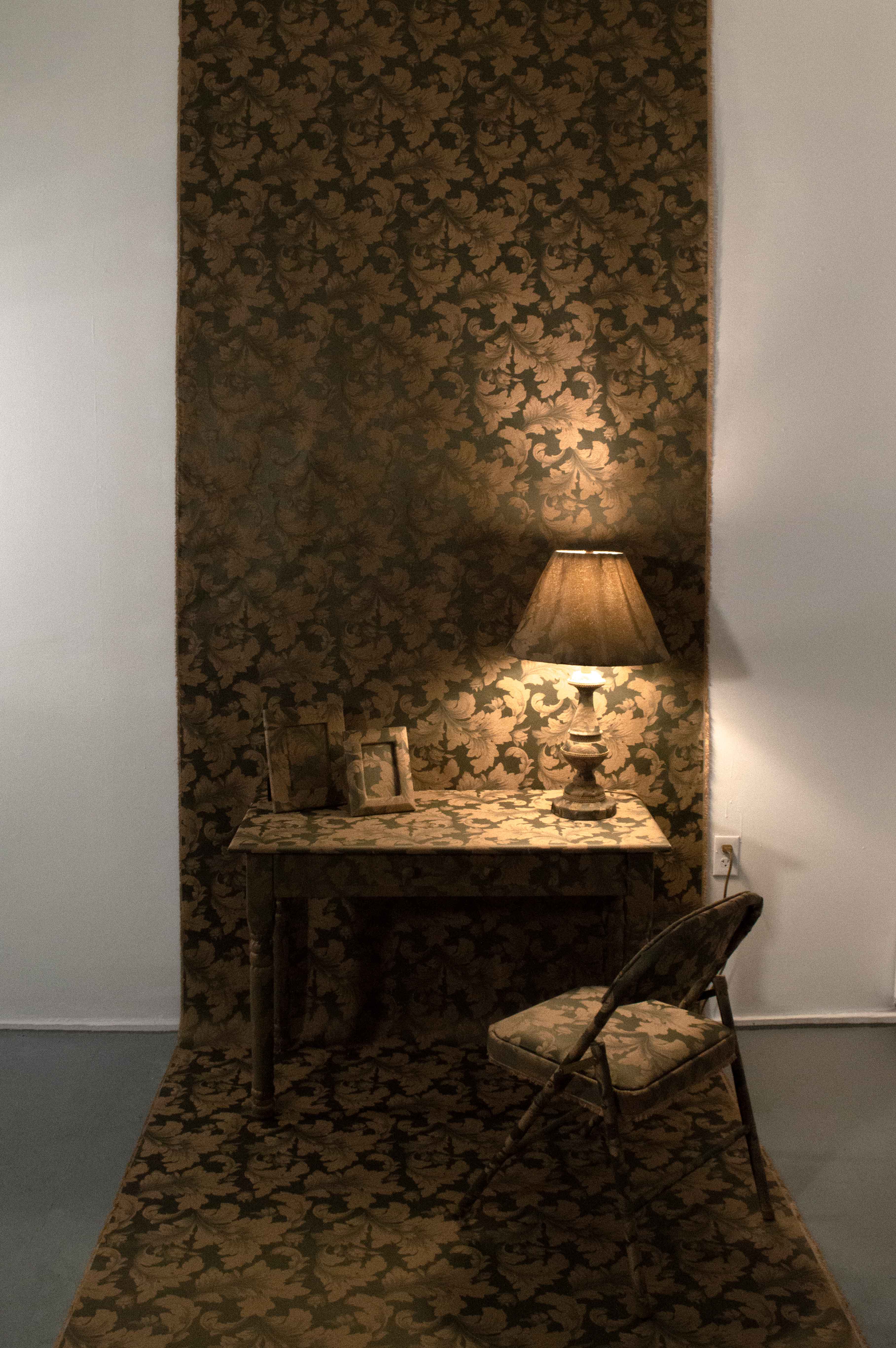 A table, a chair, two photo frames, and a lamp covered with a golden and olive green flower pattern upholstery fabric.