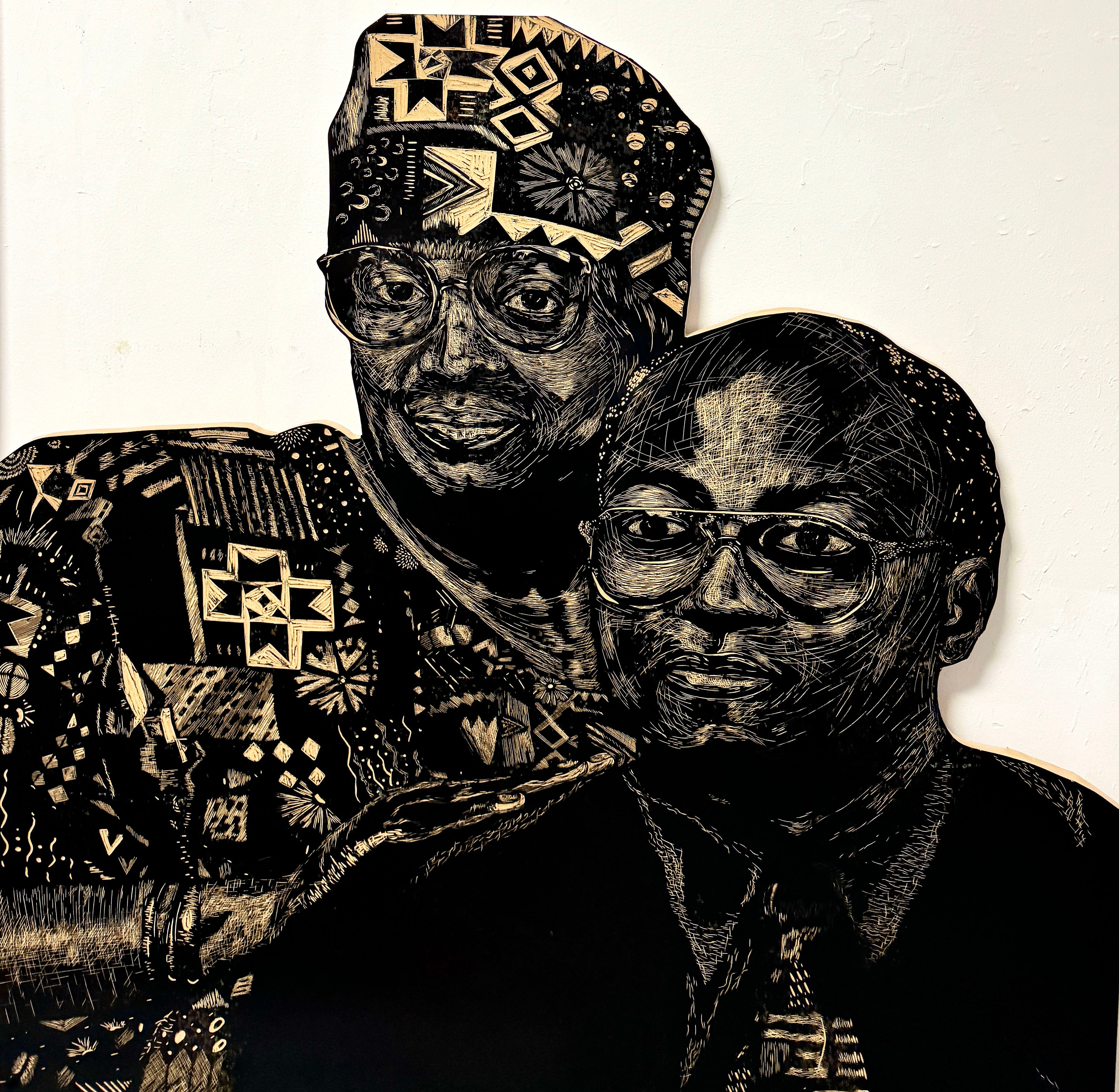 A large-scale woodcut in black and white. Portrait of the artist’s grandparents, Arthur and Cynthia Adams. Cynthia stands behind Arthur, hands on his shoulder. Cynthia wears patterned African fabric, and Arthur wears a black shirt with a patterned tie. 