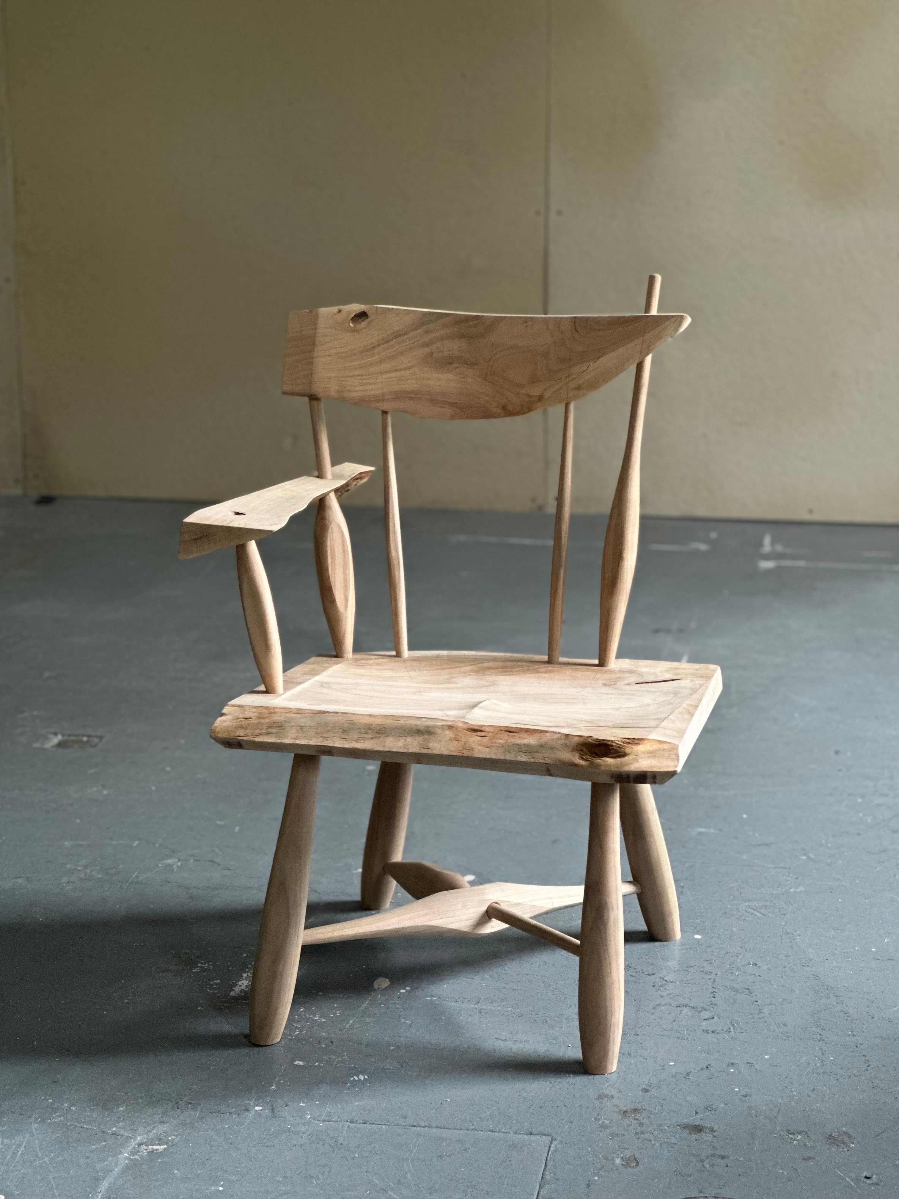 Windsor-inspired cherry chair made from a single salvaged board, featuring sculpted spindles, live edges, and visible knots. The chair emphasizes material continuity, irregularity, and the relationship between natural growth, structure, and hand-shaped form.