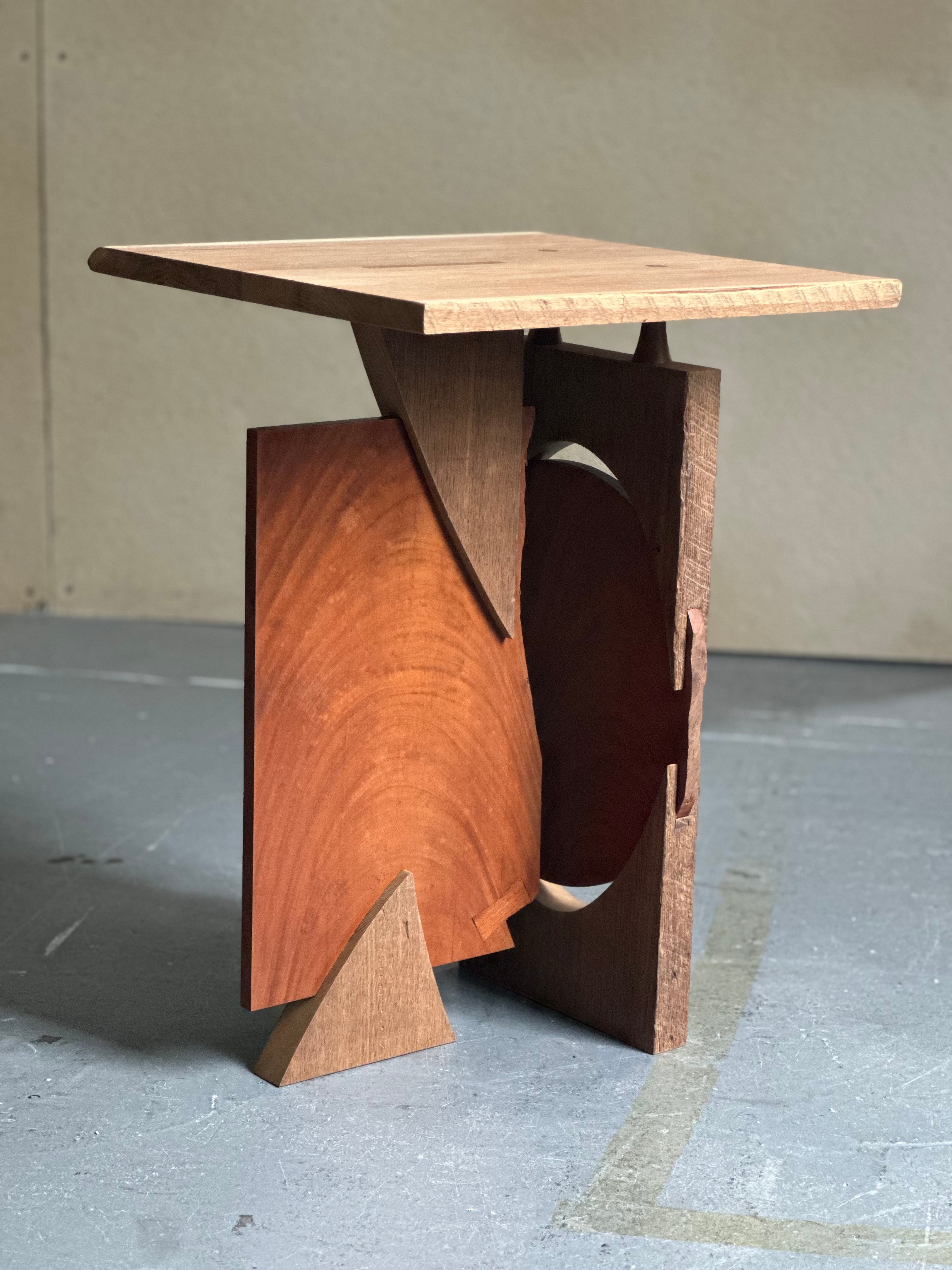 Small sculptural wooden table composed of interlocking geometric forms, contrasting wood tones, and exposed joinery.