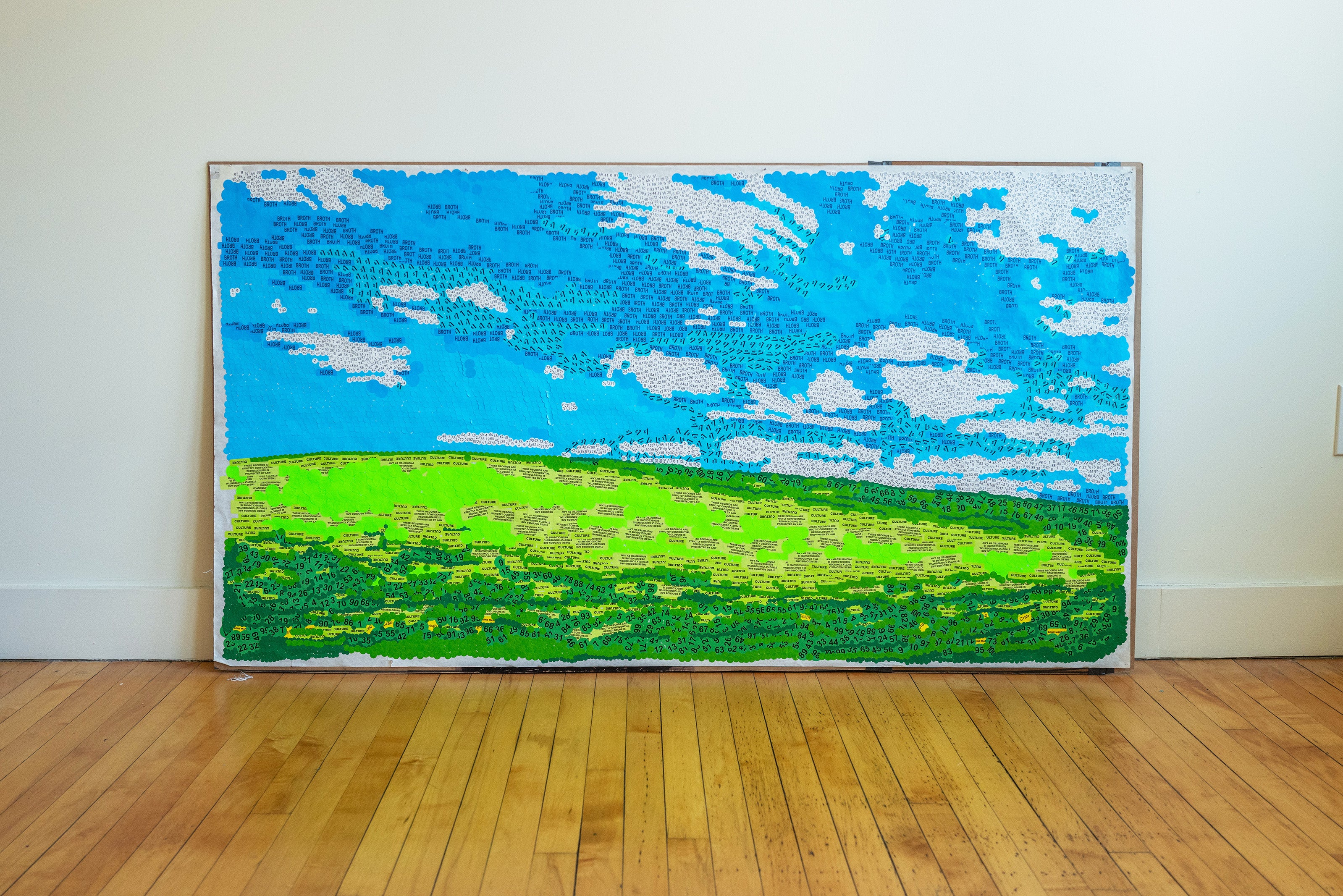 A mosaic landscape assembled from thousands of repurposed stickers — hazard warnings, food labels, confidentiality markers — evoking pointillism. From afar, nature; up close, the symbols of automated consumption.