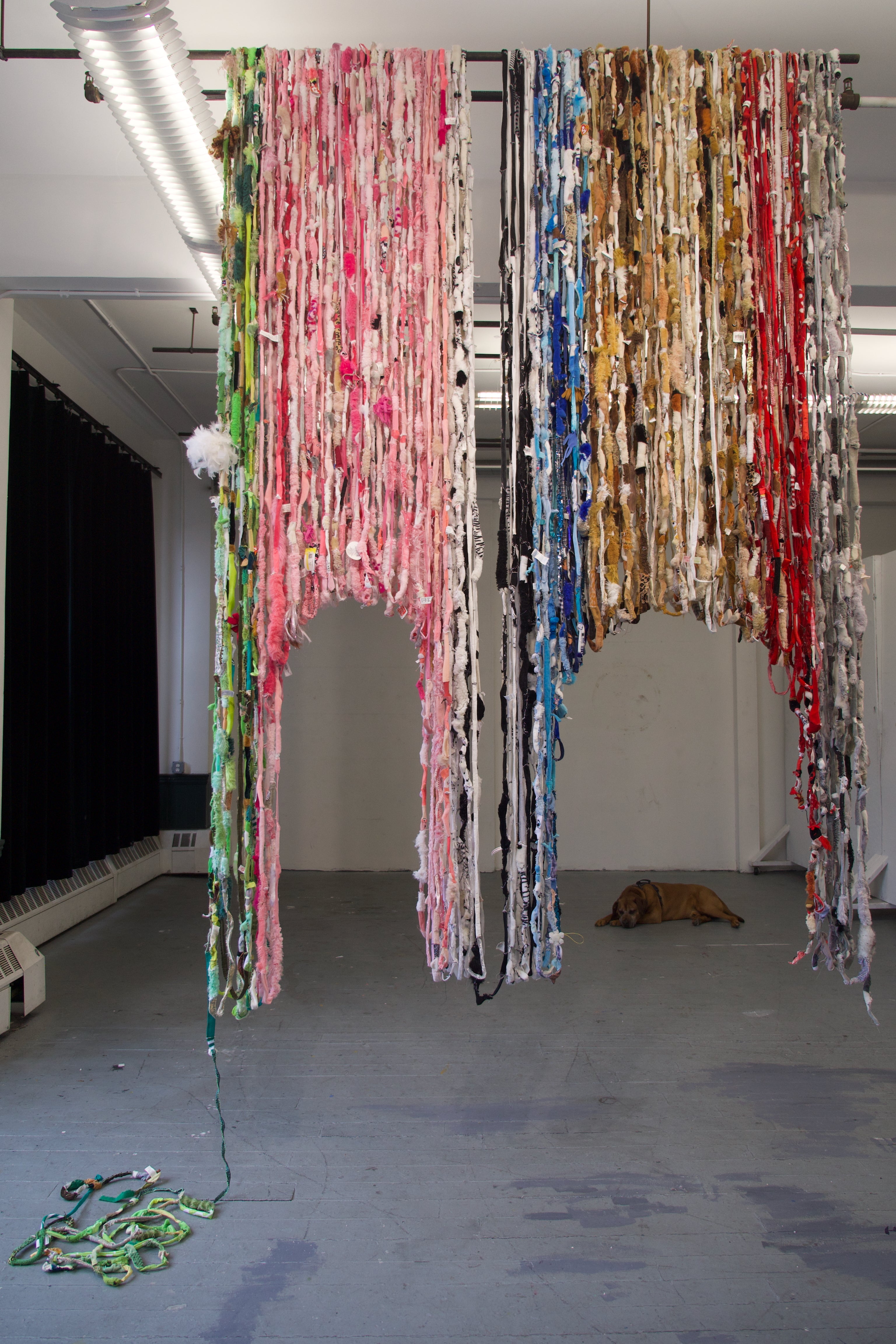 Stuffed animals cut up and sewn together into rope. Color coordinated in sections (from left to right): green, pink, black and white, blue, brown, red, and grey. The rope is looped repeatedly from the ceiling