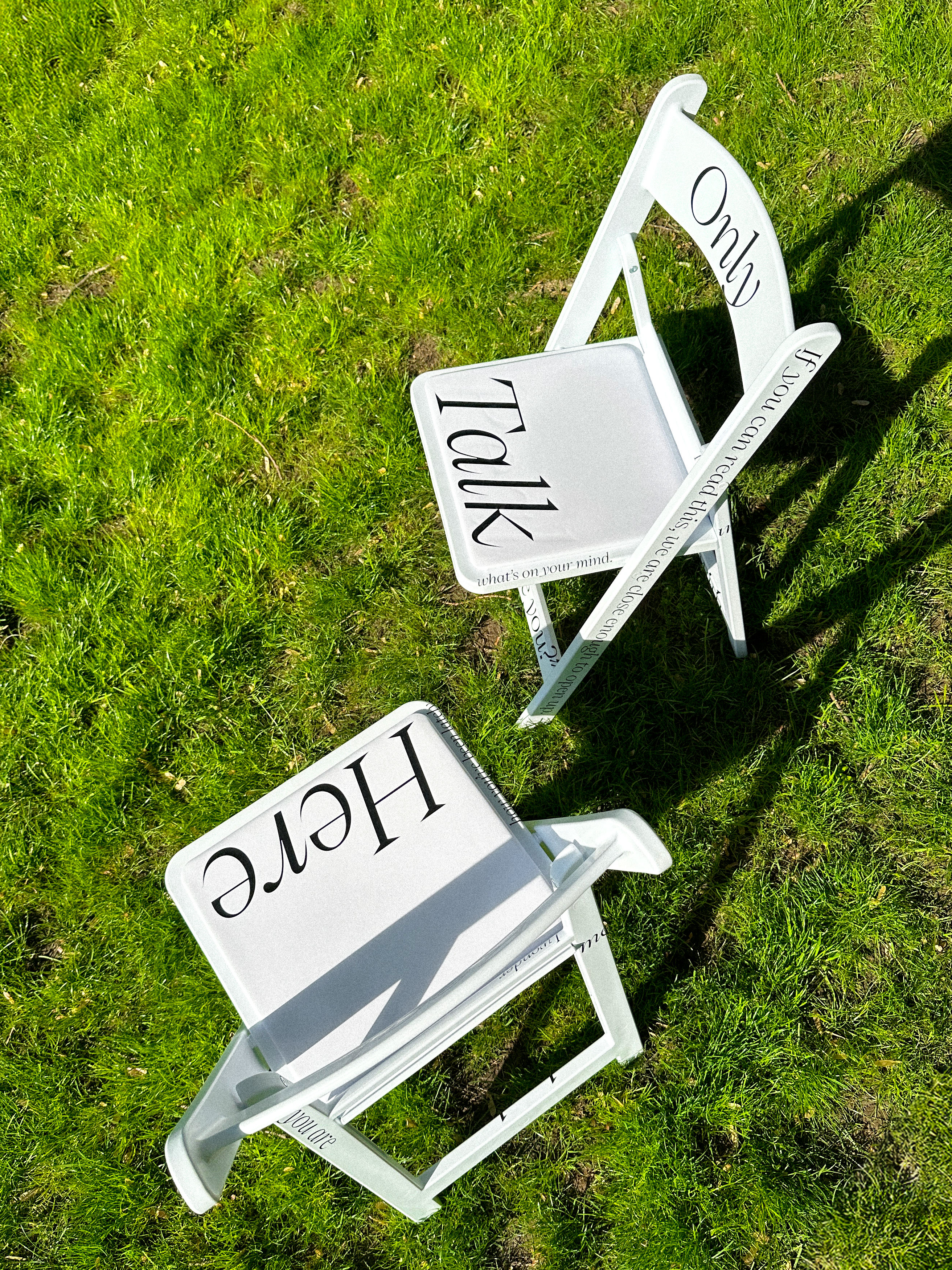 Two white chairs placed outdoors, printed with black text showing various conversation prompts.