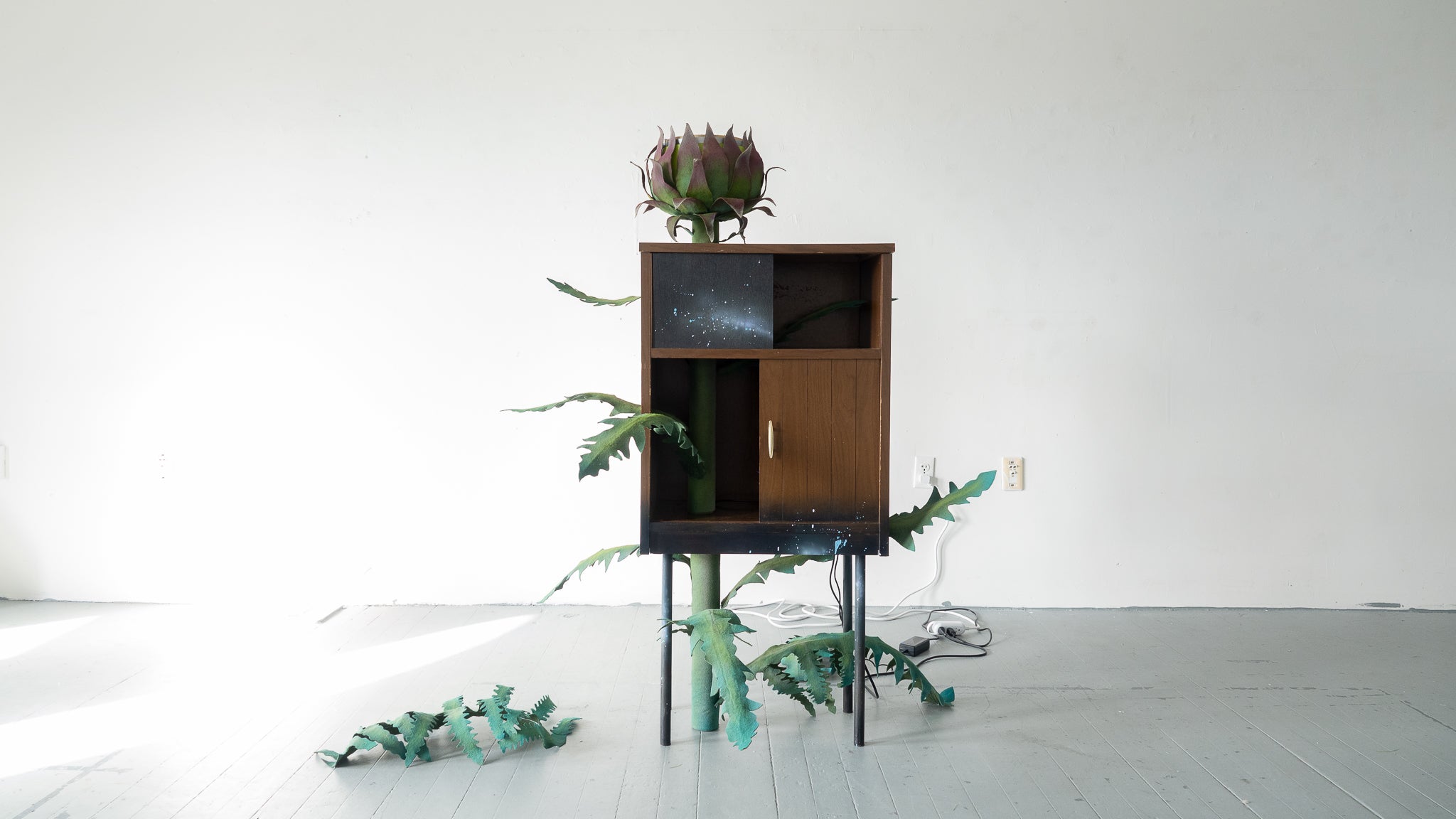 Cabinet sculpture with green felt leaves and a flower-like form emerging from the top.
