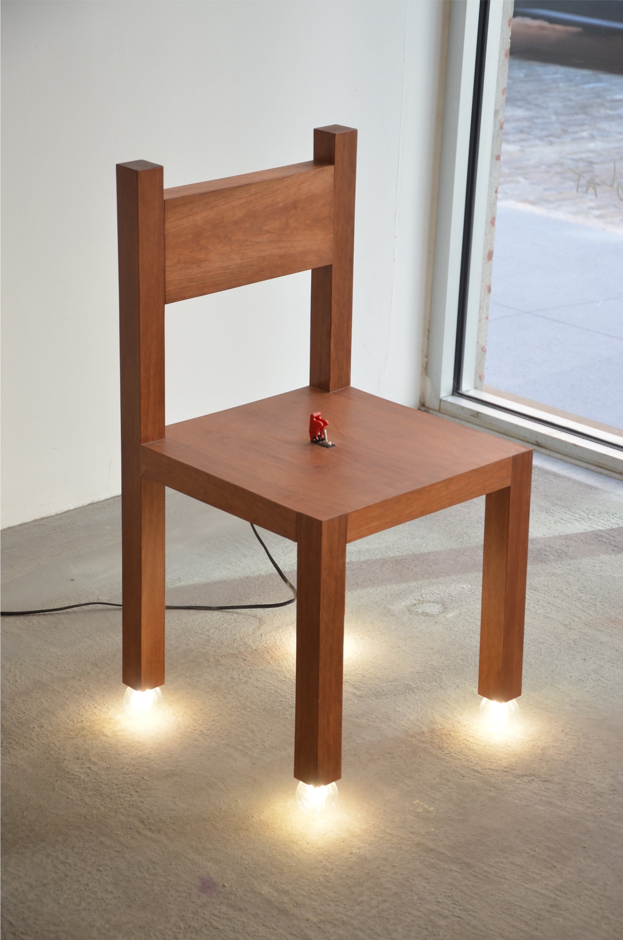 Cherry Chair with four light bulbs as its feet and a red switch in the seat, combining a chair and a lamp.