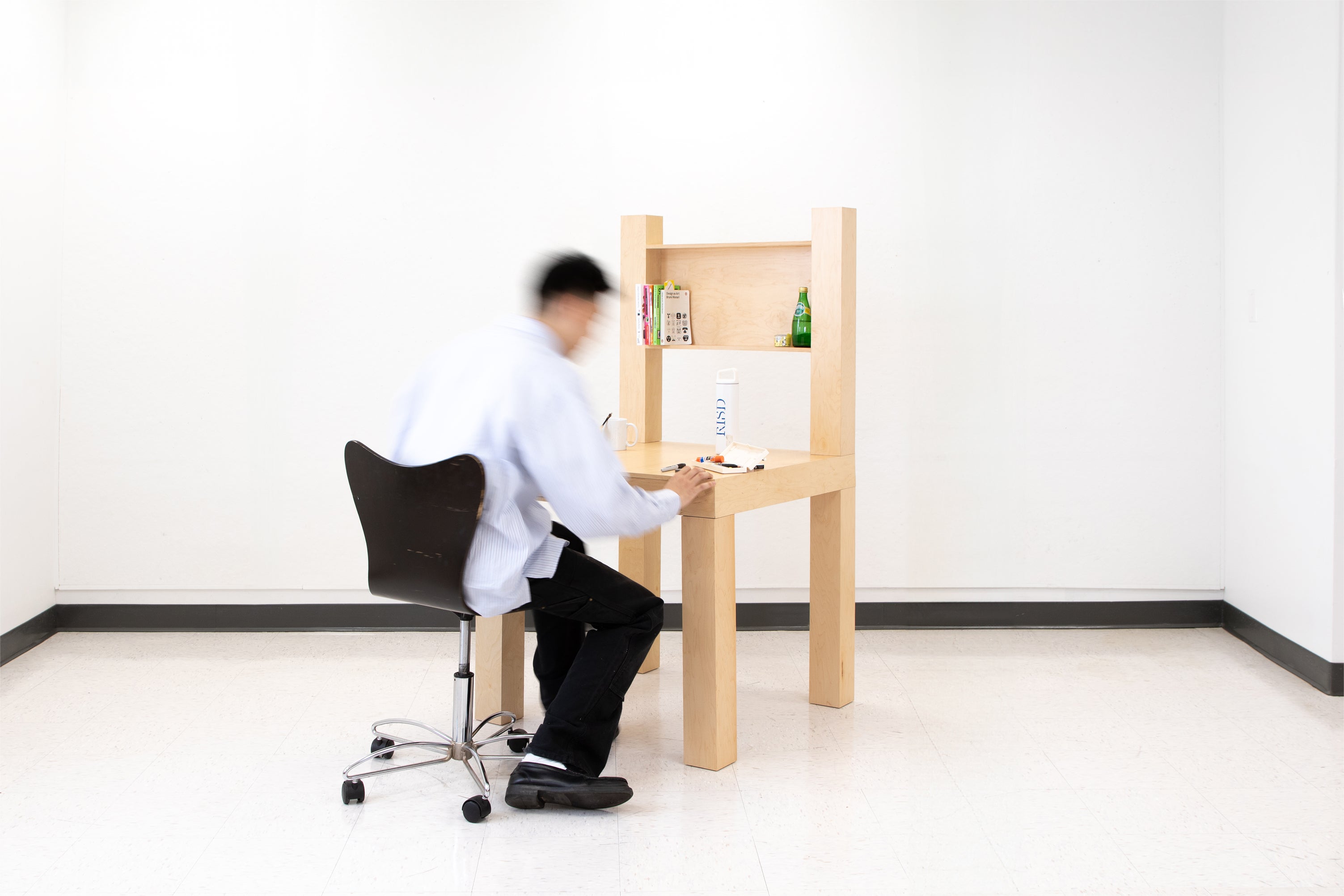 A large wooden chair-shaped object with a desk surface, drawer, and shelving, functioning as a desk instead of a chair.
