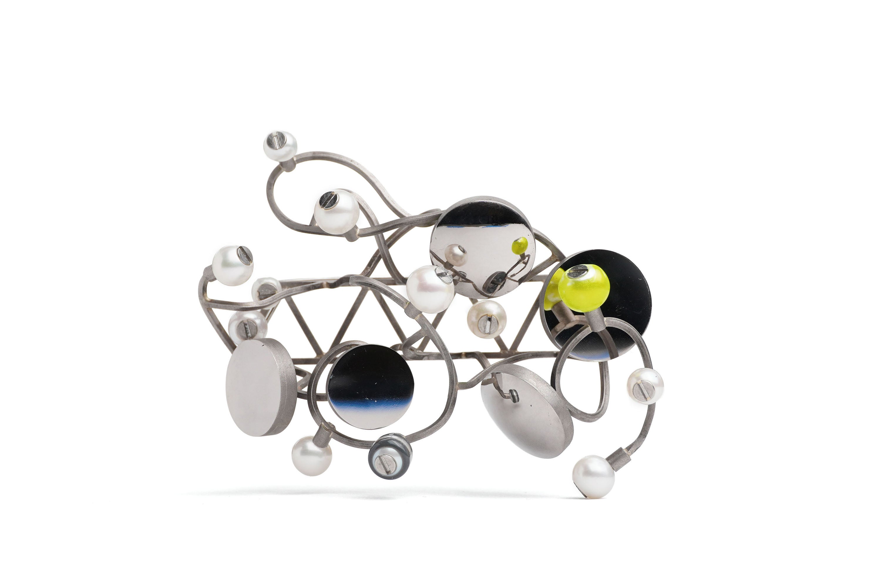 A brooch loosely in the shape of a triangular truss with branching and twisted lengths of wire wrapped around it. Circular mirror panels and pearls are bolted along its length with screws. On a white background.
