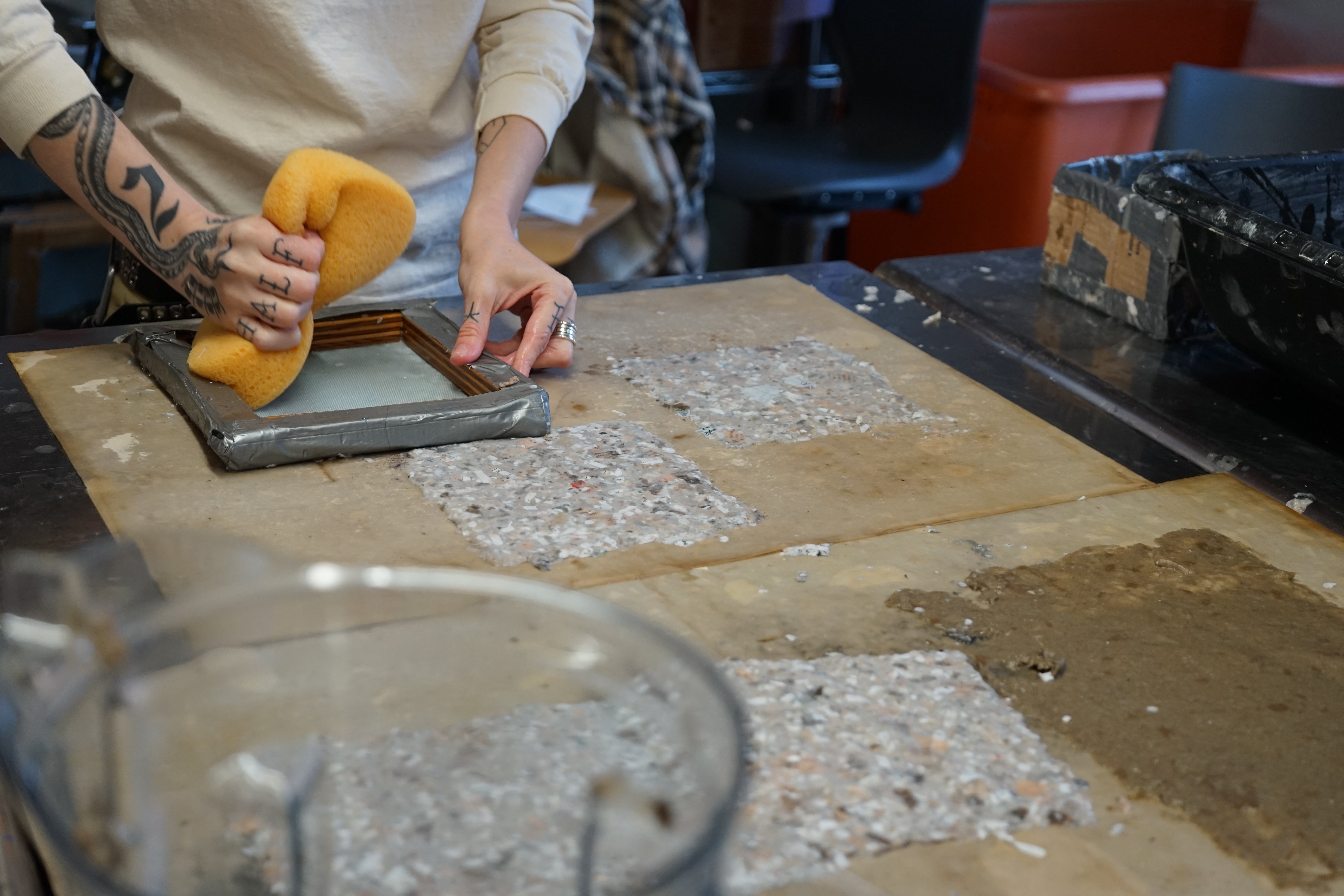 Image of hand holding sponge to absorb water from paper which has just been applied with a deckle.
