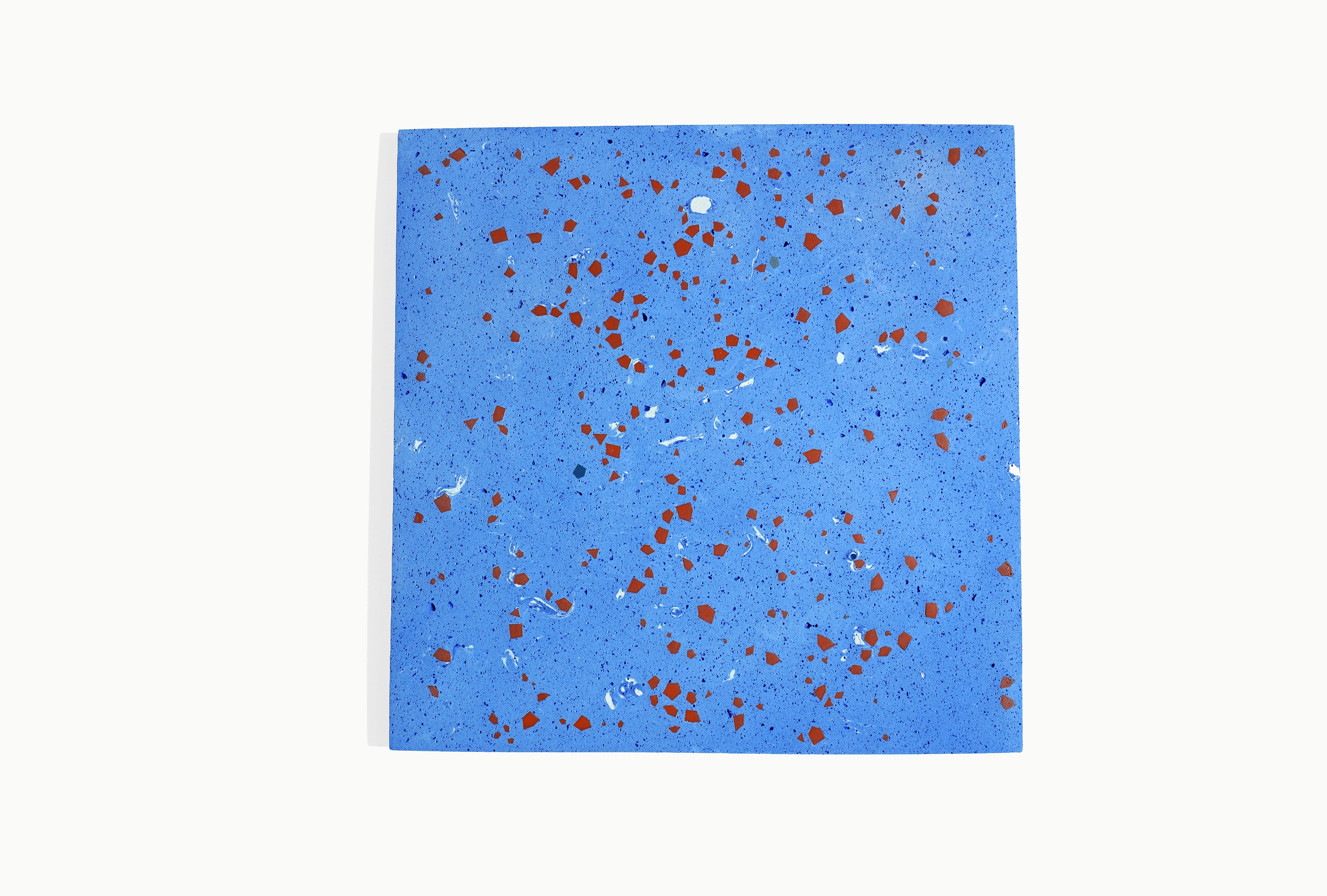 A single square pale blue terrazzo tile embedded with geometric fragments scattered across its surface.