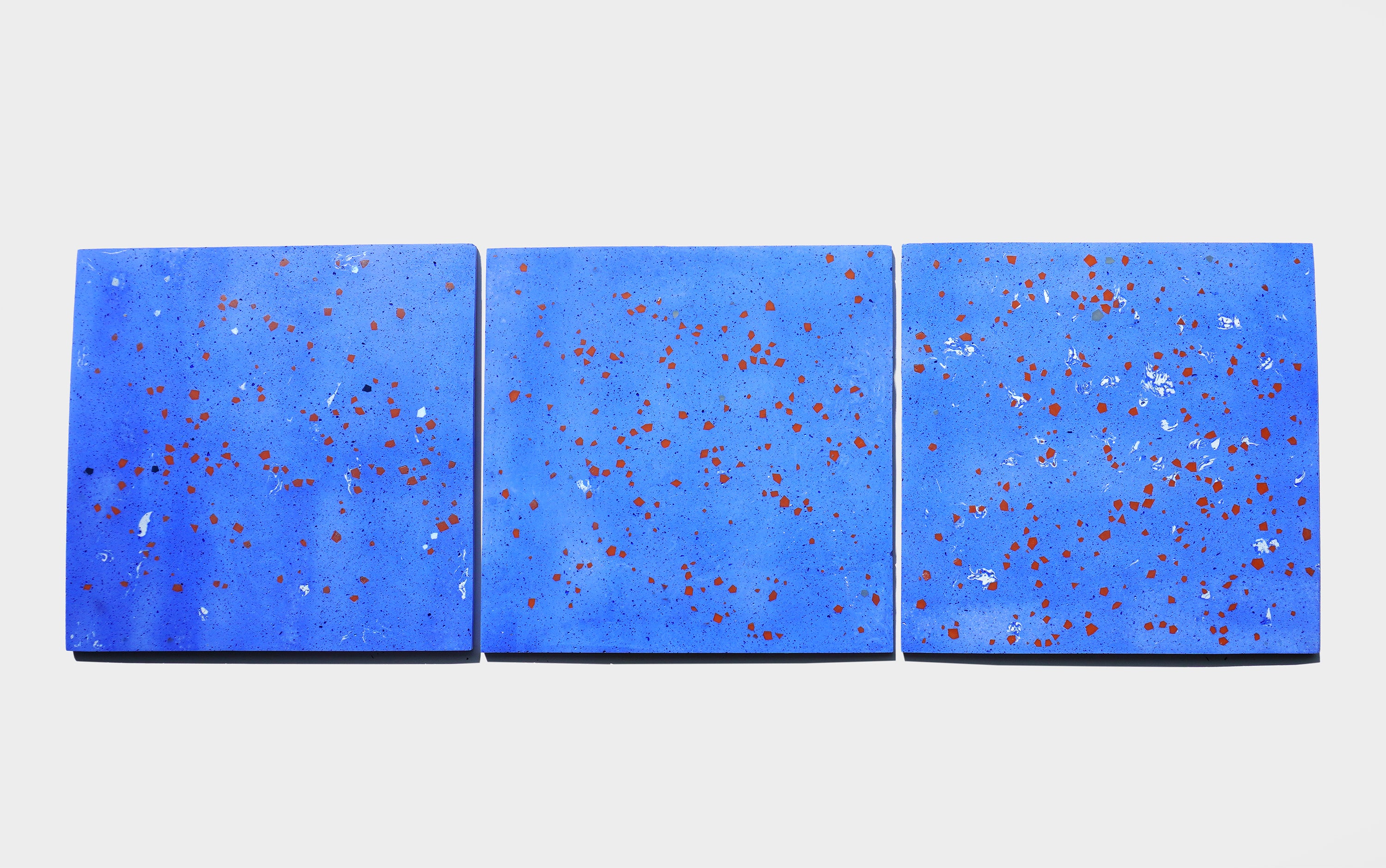 Three square pale blue terrazzo tiles arranged side by side, each embedded with scattered colored geometric fragments of varying sizes and shapes.