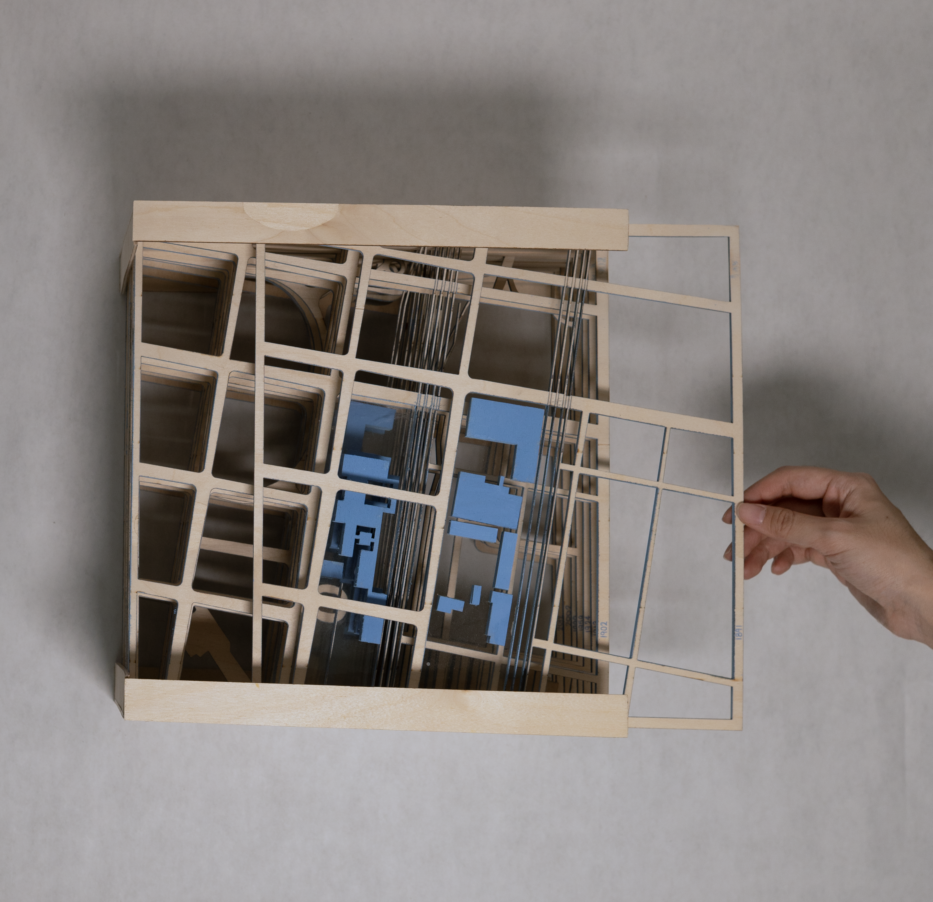 Hand pulling square wooden map with blue buildings to reveal maps of later years layered beneath.