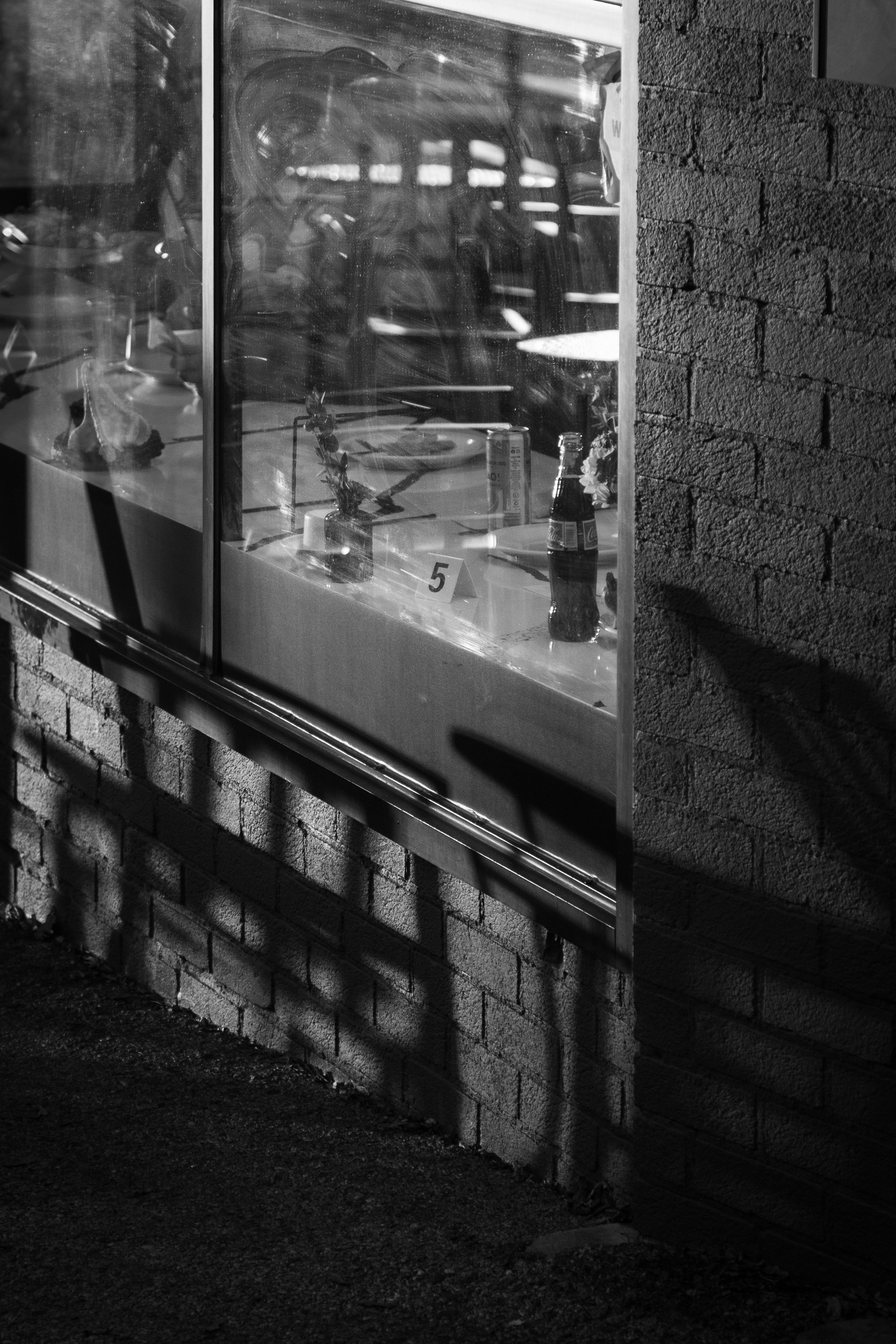 Restaurant window reflection showing a order number and a Coke bottle, black and white photography with brick facade.