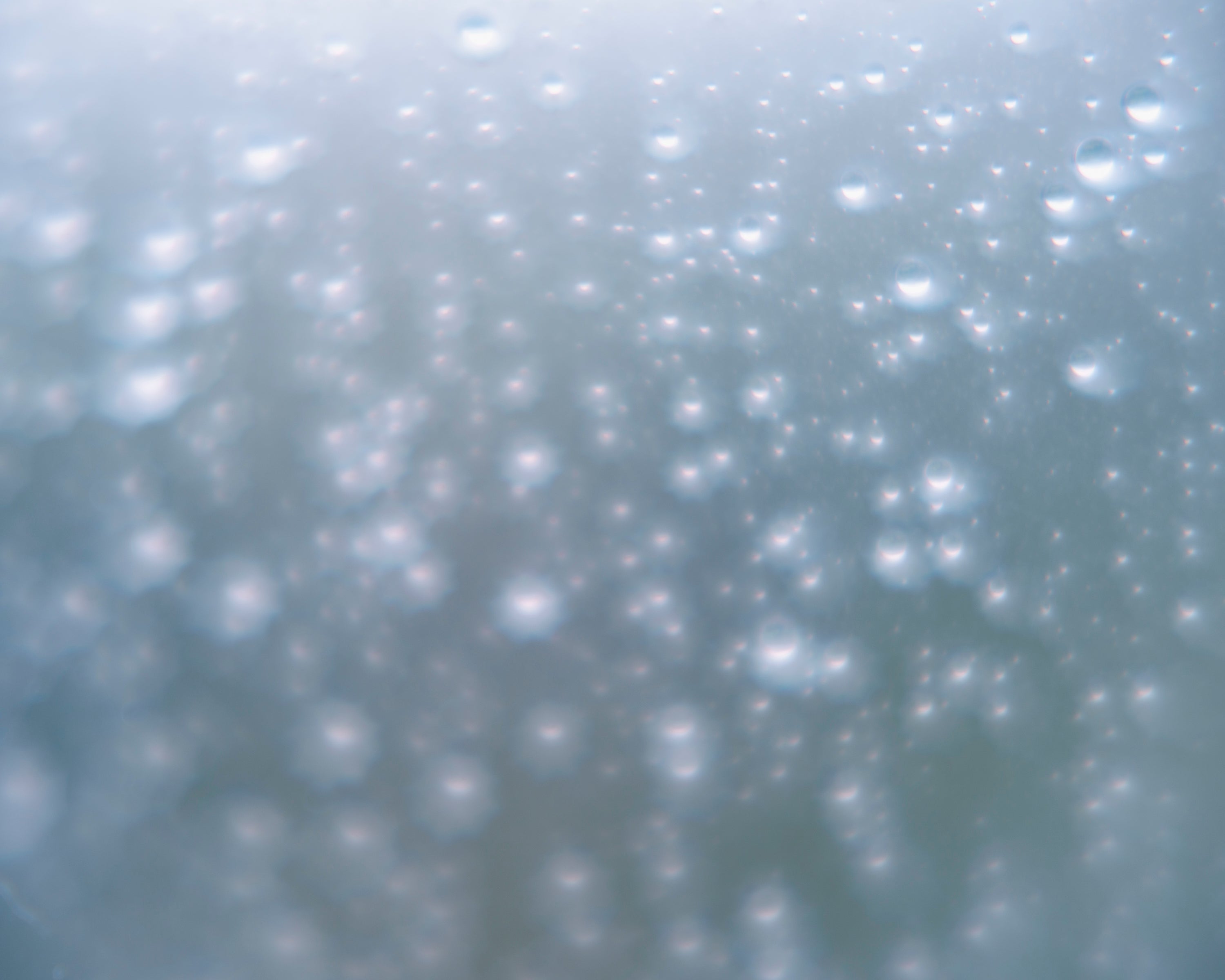 Color photograph of blurry raindrops, suspended in watery blue background.