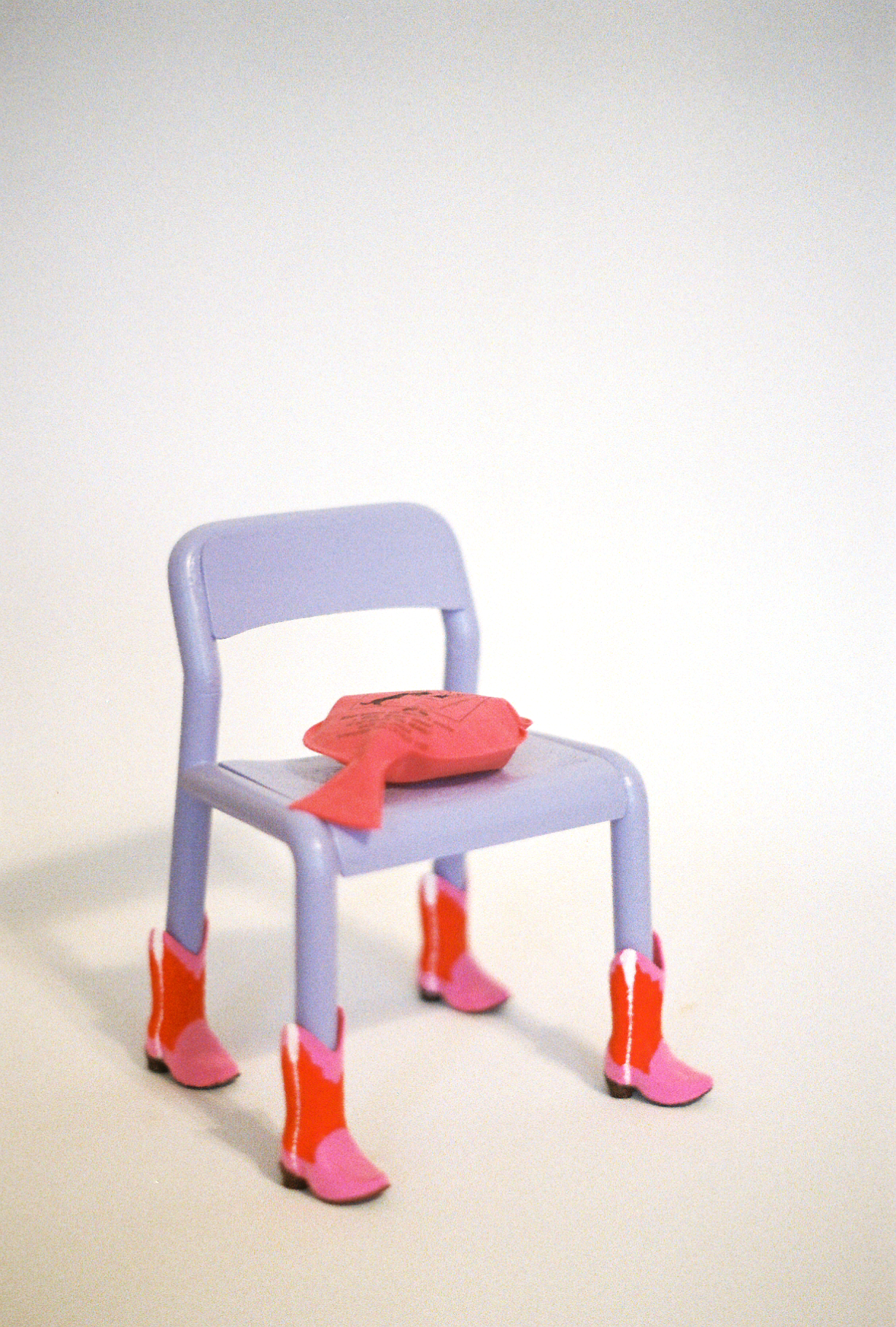 35mm film photograph of a 7" model of a lavender painted Ikea chair wearing pink and red cowboy boots and a whoopee cushion on the seat.