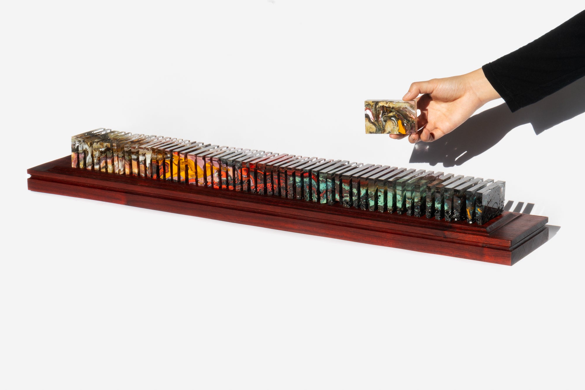 Fifty-three polished glass slices displayed on a long padauk platform showing both gaps and continuation at the same time. 