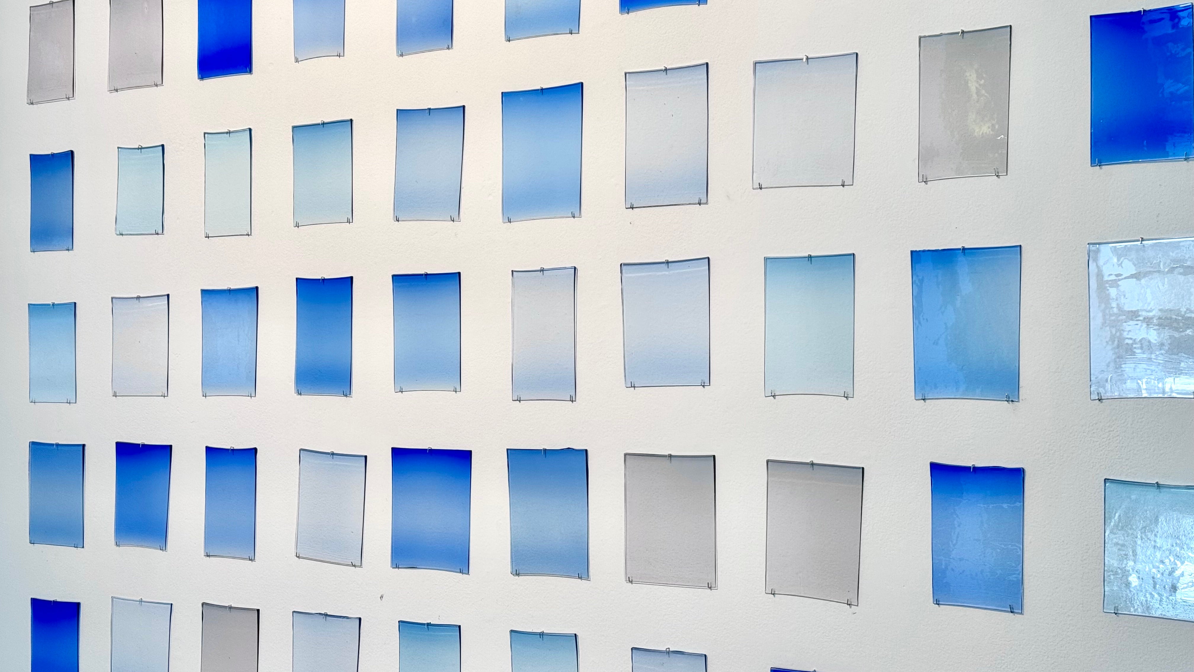 Grit of rectangular glass panels mounted on a wall, each showing subtle variations of blue gradients and transparency.