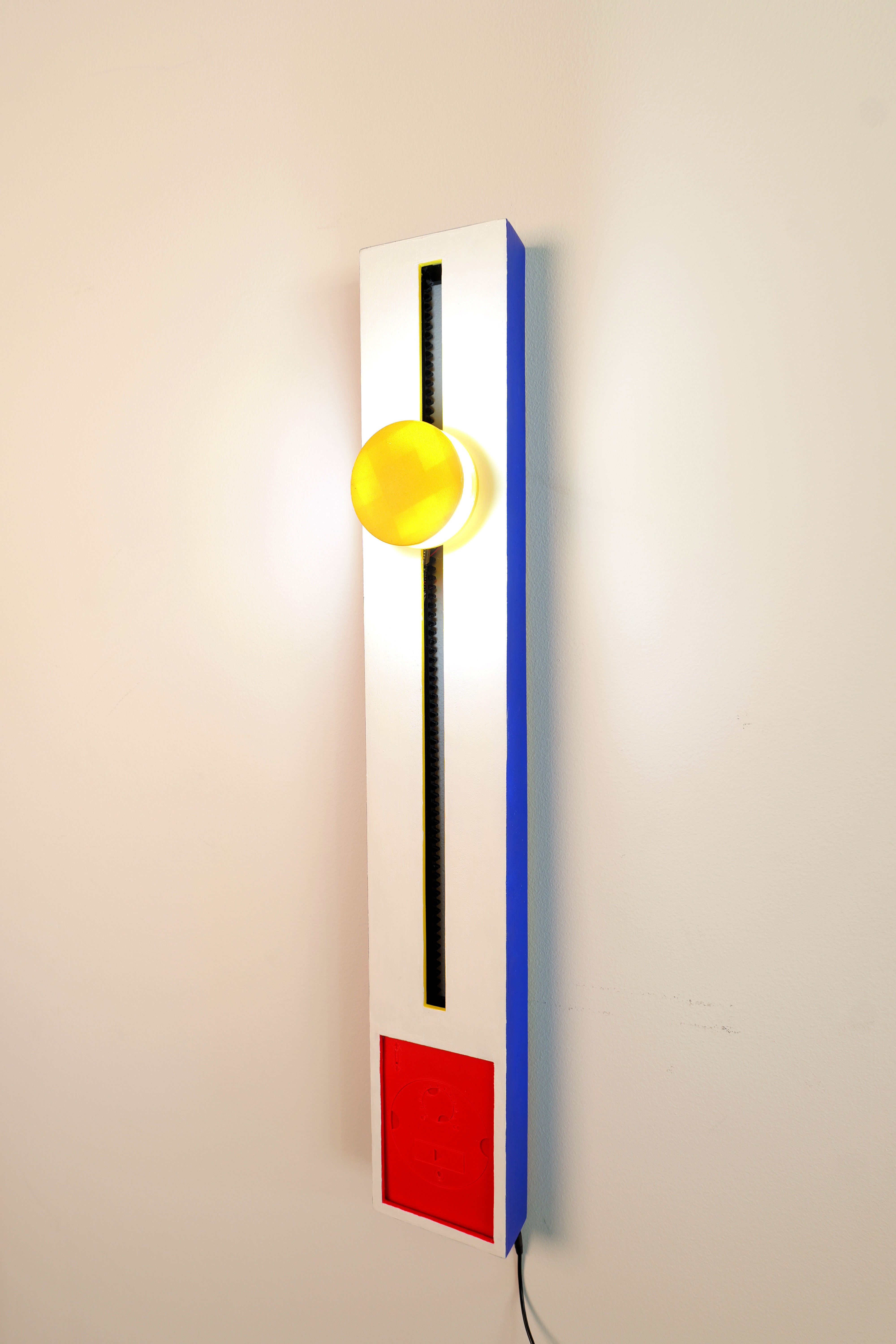 A white and blue vertical rectangle with a yellow cylindrical light, red panel, and blue track.