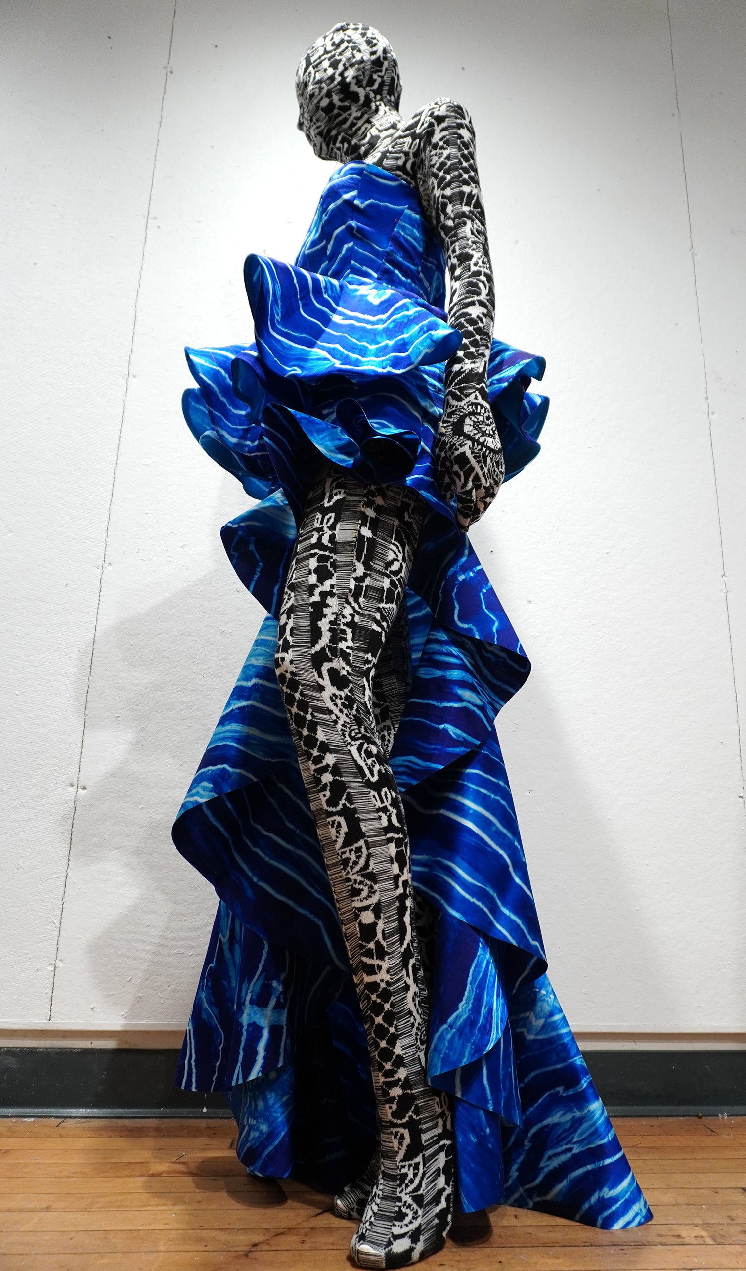 Mannequin wearing sculptural blue silk dyed dress with wave-like ocean patterns over black-and-white jacquard knitted bodysuit.