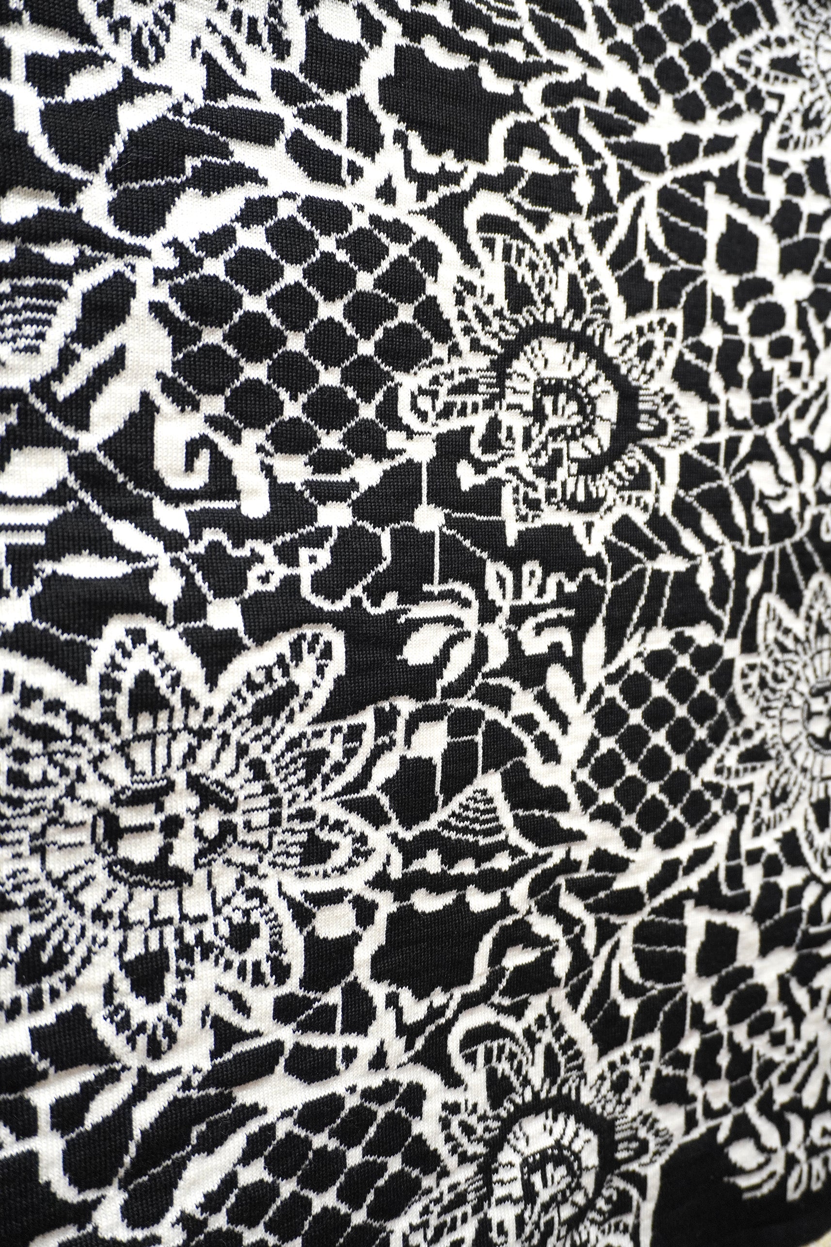 Close-up of black-and-white jacquard knitted textile resembling lace, with floral motifs and shells