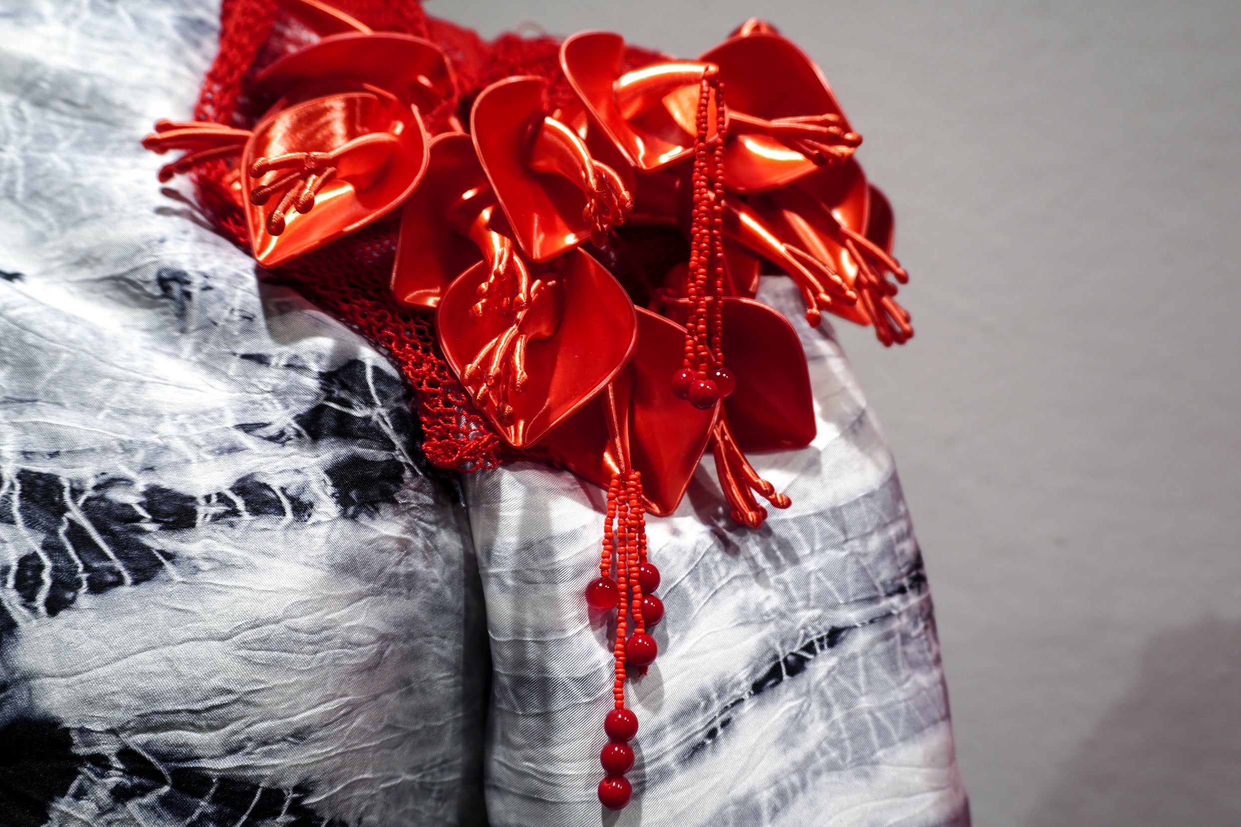 Close-up of glossy red 3D-printed ceibo flowers with beaded strands over black-and-white hand-dyed silk textile.