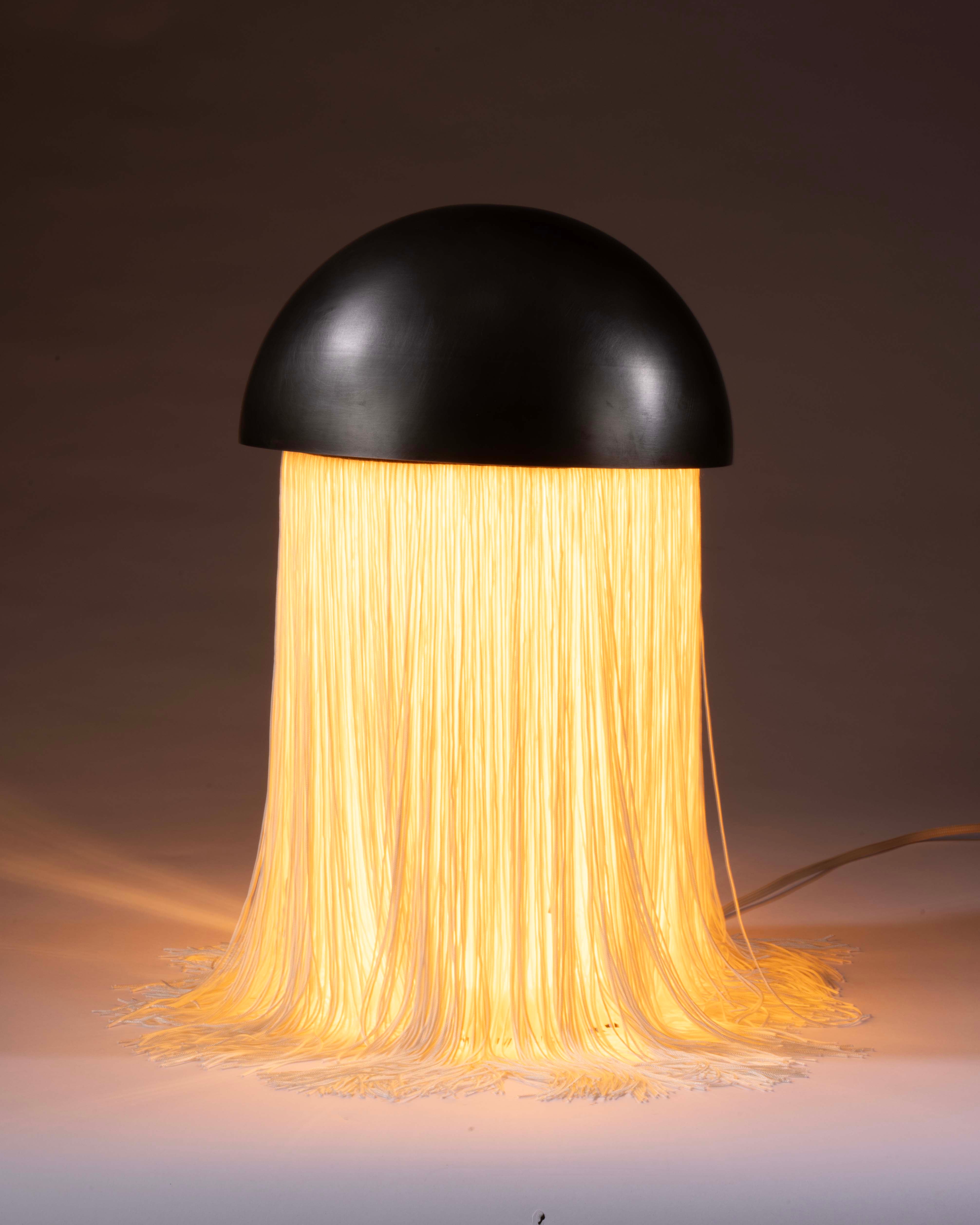 A table lamp with ivory fringe draping from a steel dome. 