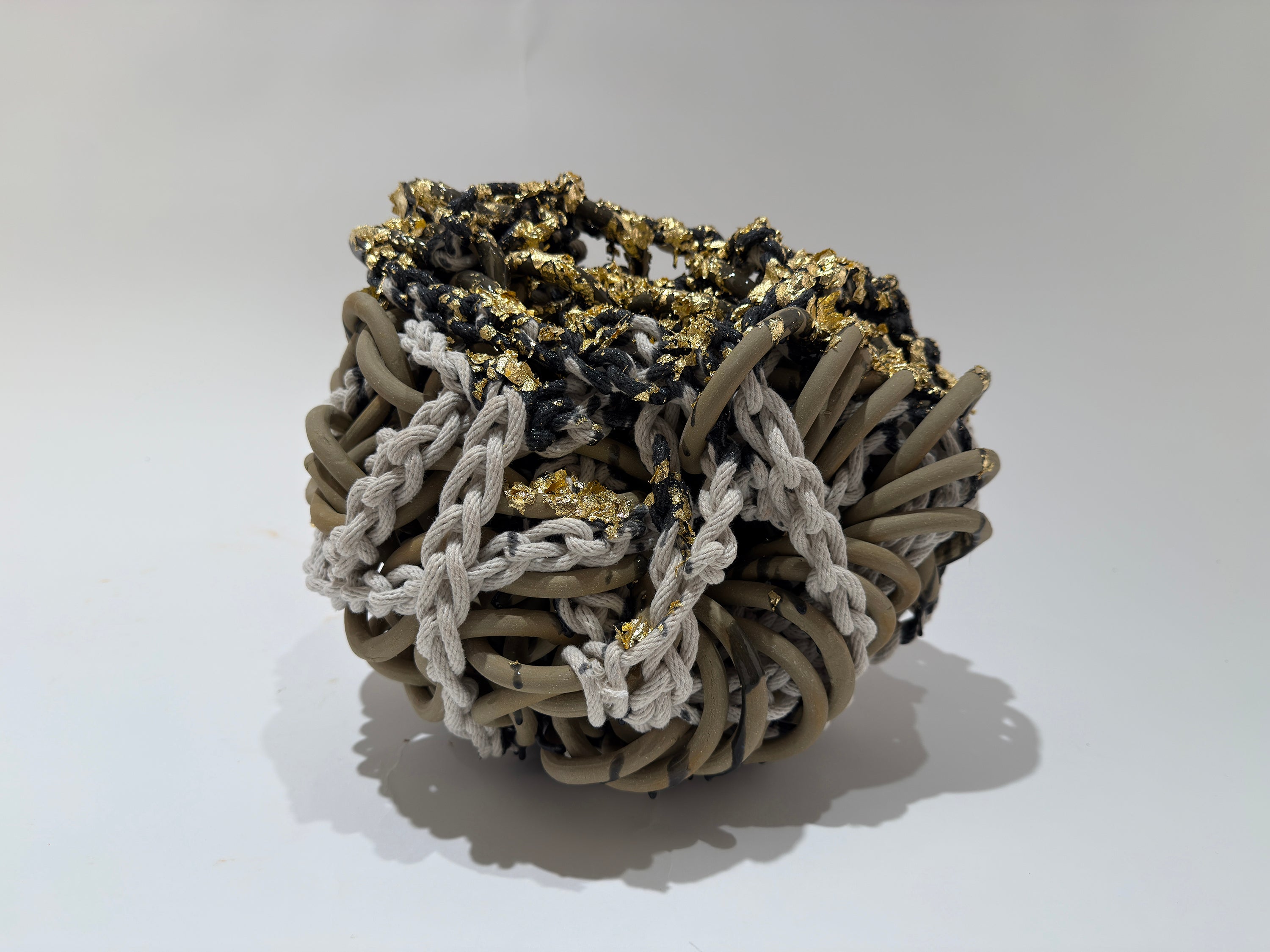 Smooth tan chainmail is wrapped in white rope.  On top blue latex is dripped and upon it is small bits of gold leaf sparkleing in a very dense work.