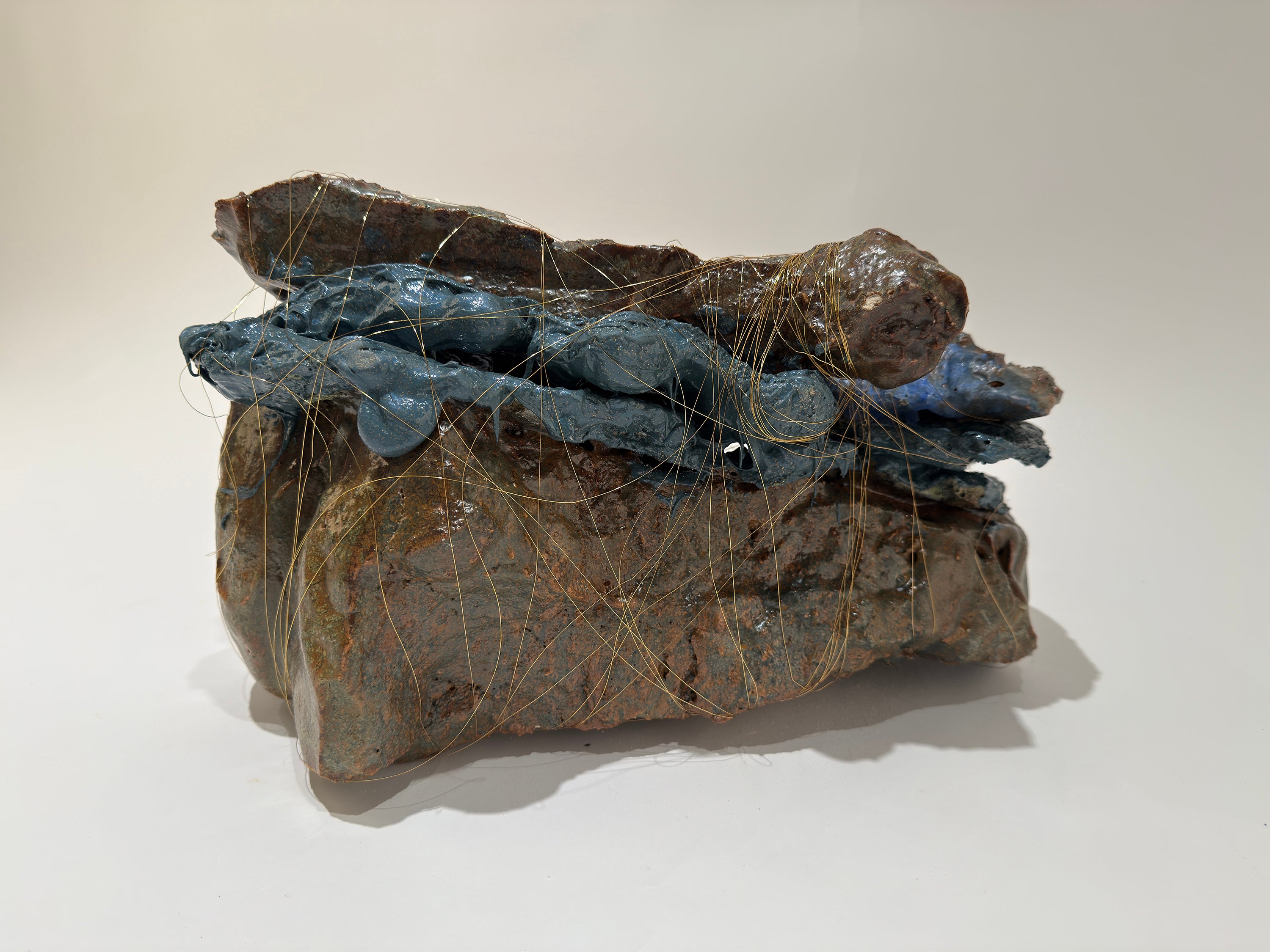 Three large smooth shiny glazed rock like pieces are faceted together with purple rubber.  The entire piece is wrapped with small copper thread as thin a hair.