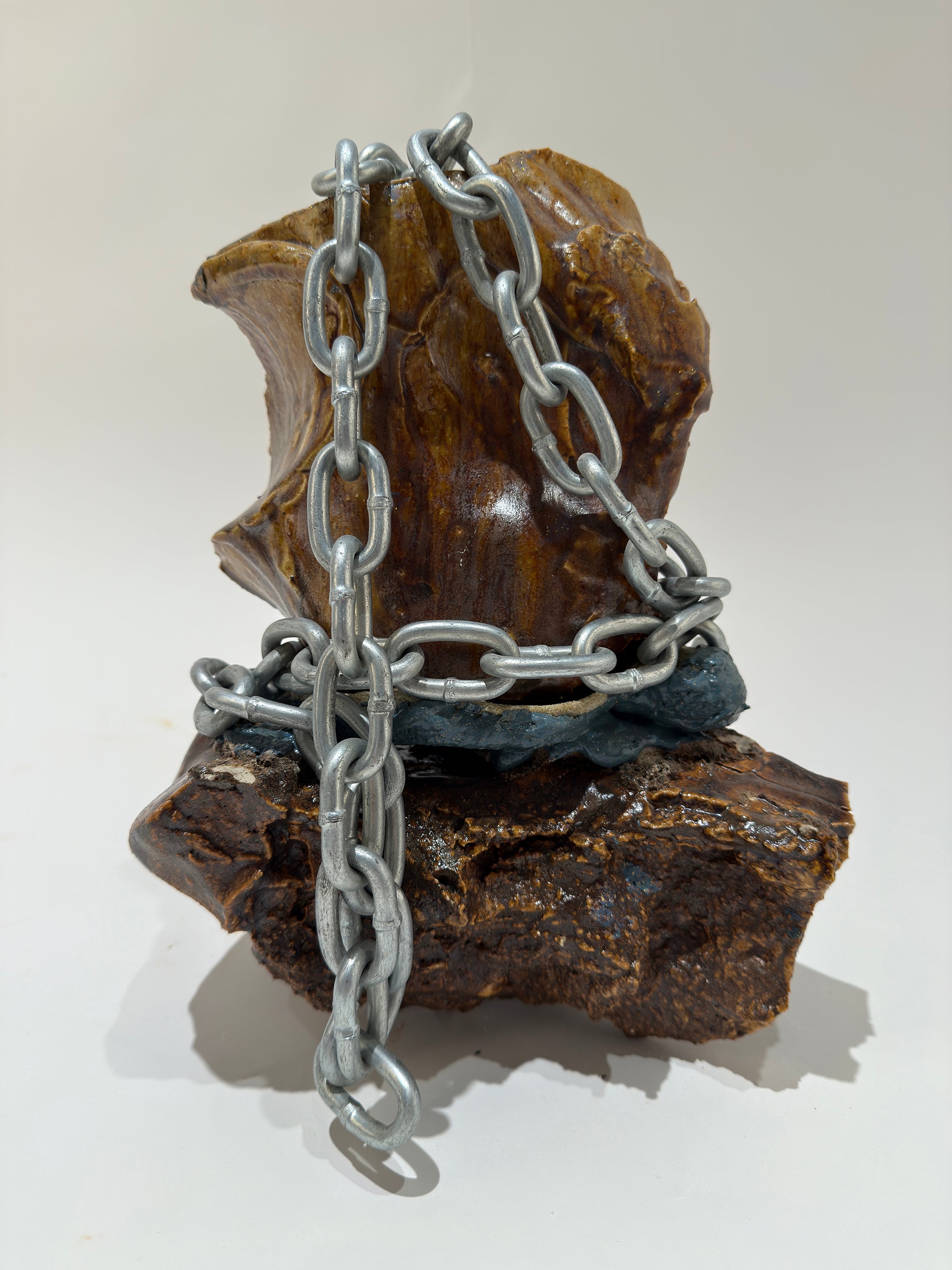 Several smooth rock like ceramic shards are faceted together with rubber.  A large steel chain wraps around the piece loosely but adds some weight to the object.