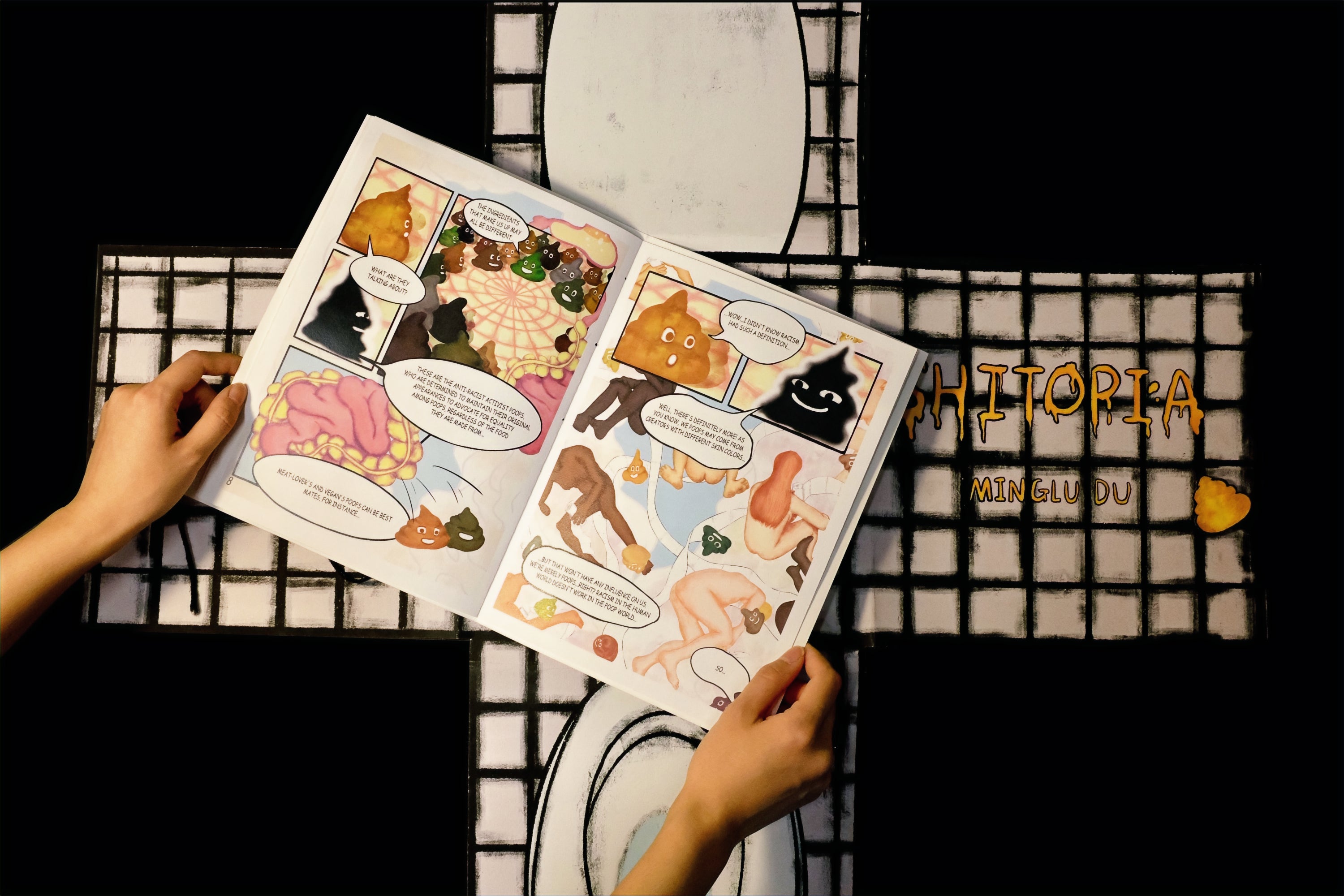 An opened interior page from the comic book Shitopia is placed on top of the foldable toilet-shaped cover.