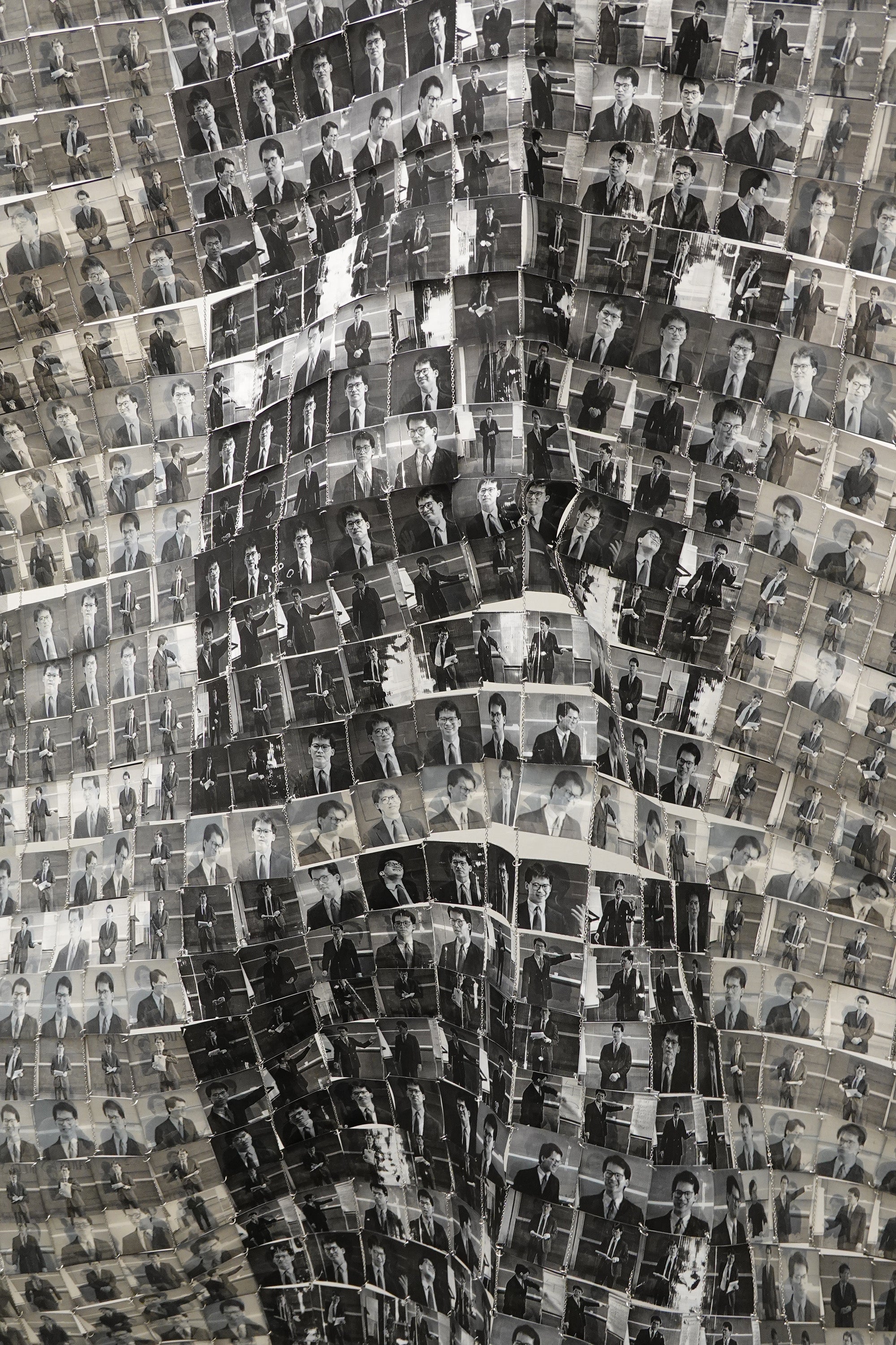 Close up image of black and white paper tiles that each have a portrait of a man in glasses.