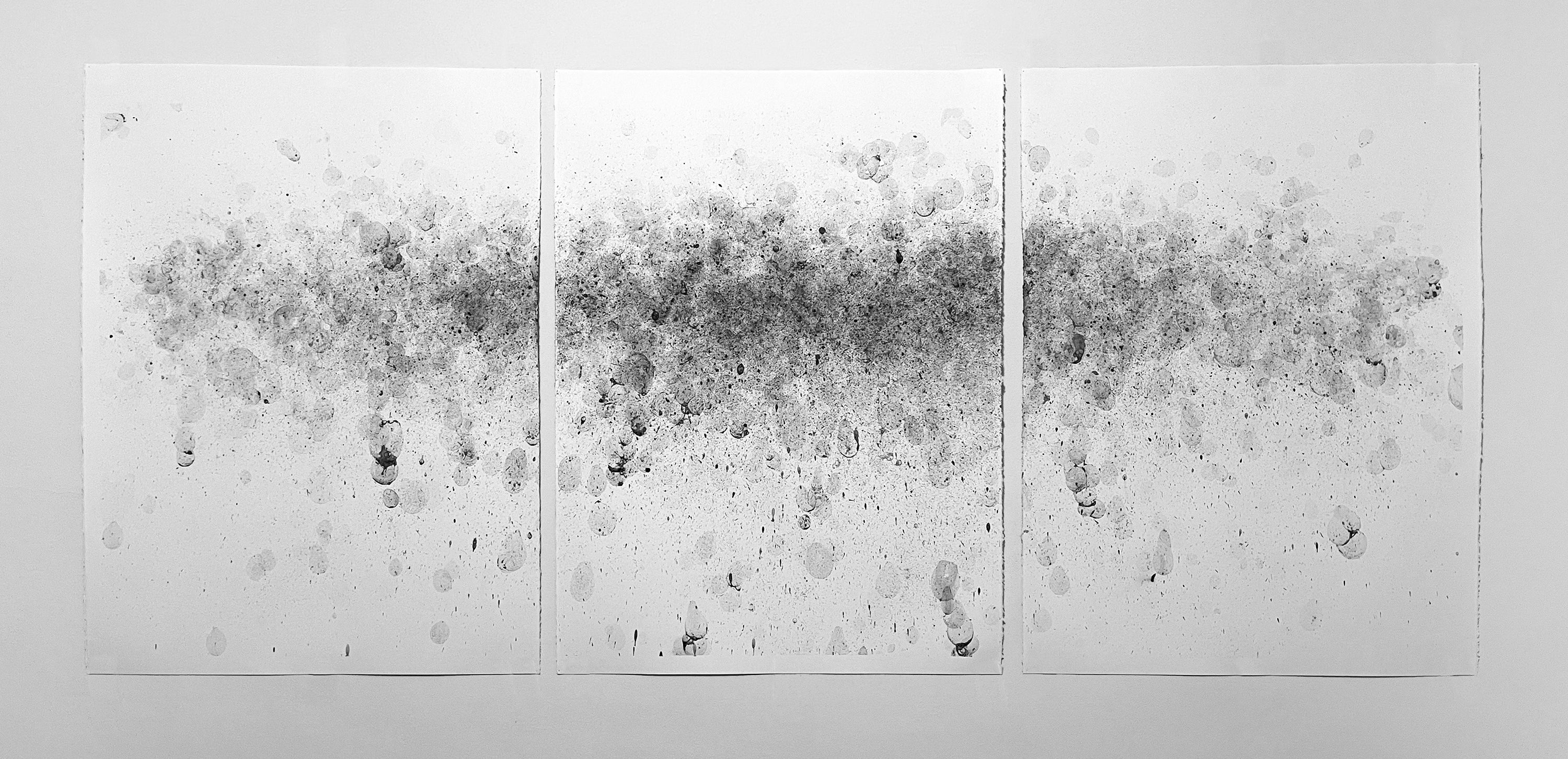 Three-panel charcoal drawing on white paper with a horizontal cloud of gray-black speckles, soft circular stains, and scattered marks fading outward across the surface.