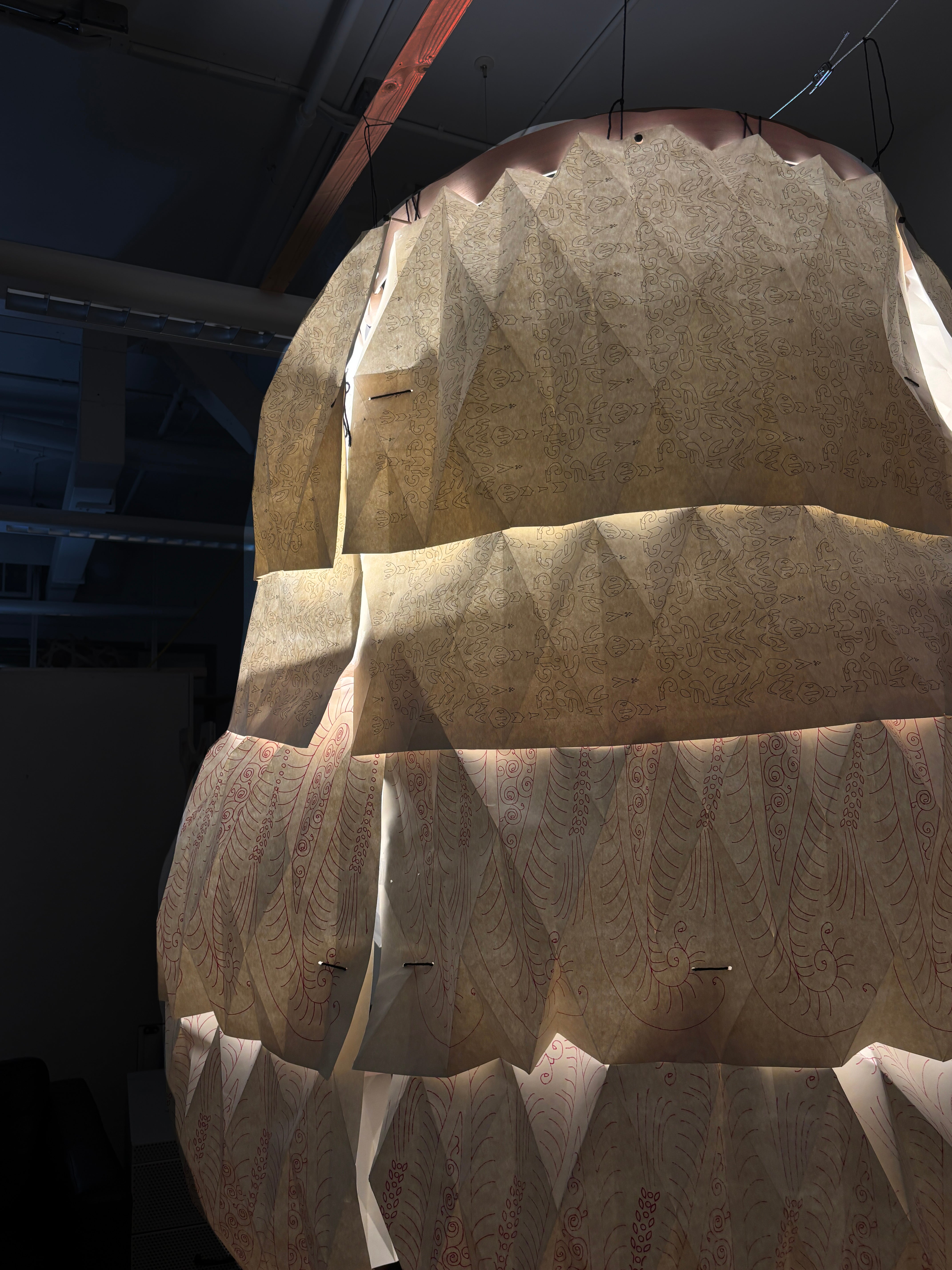 Paper Structure showcasing cascading paper which is layered and hung from the ceiling. Each page features textile designs that have been drawn onto the surface of the sheets.