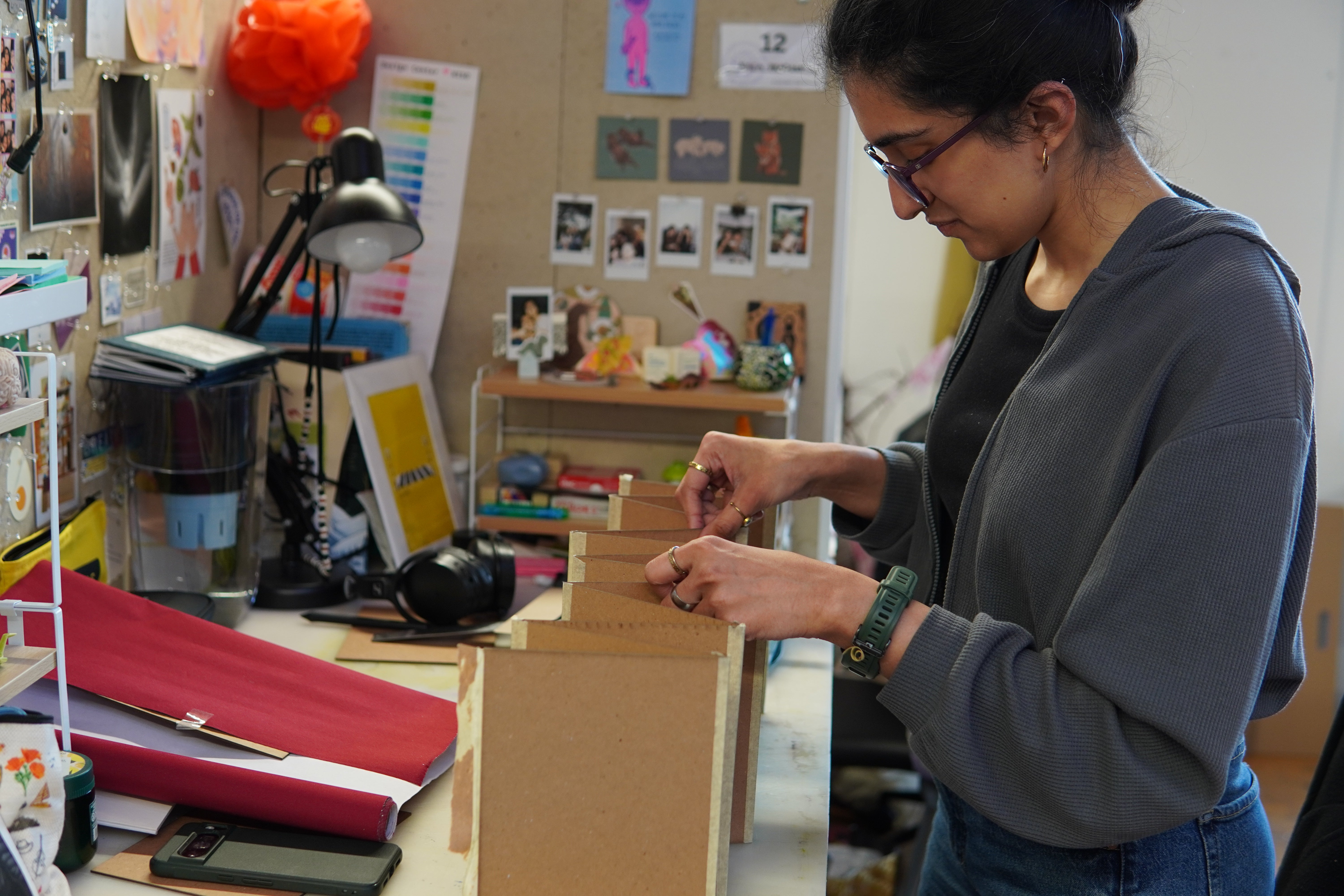 Image shows artist arranging an accordion fold mockup book made of scrap material as a prototype for her final.
