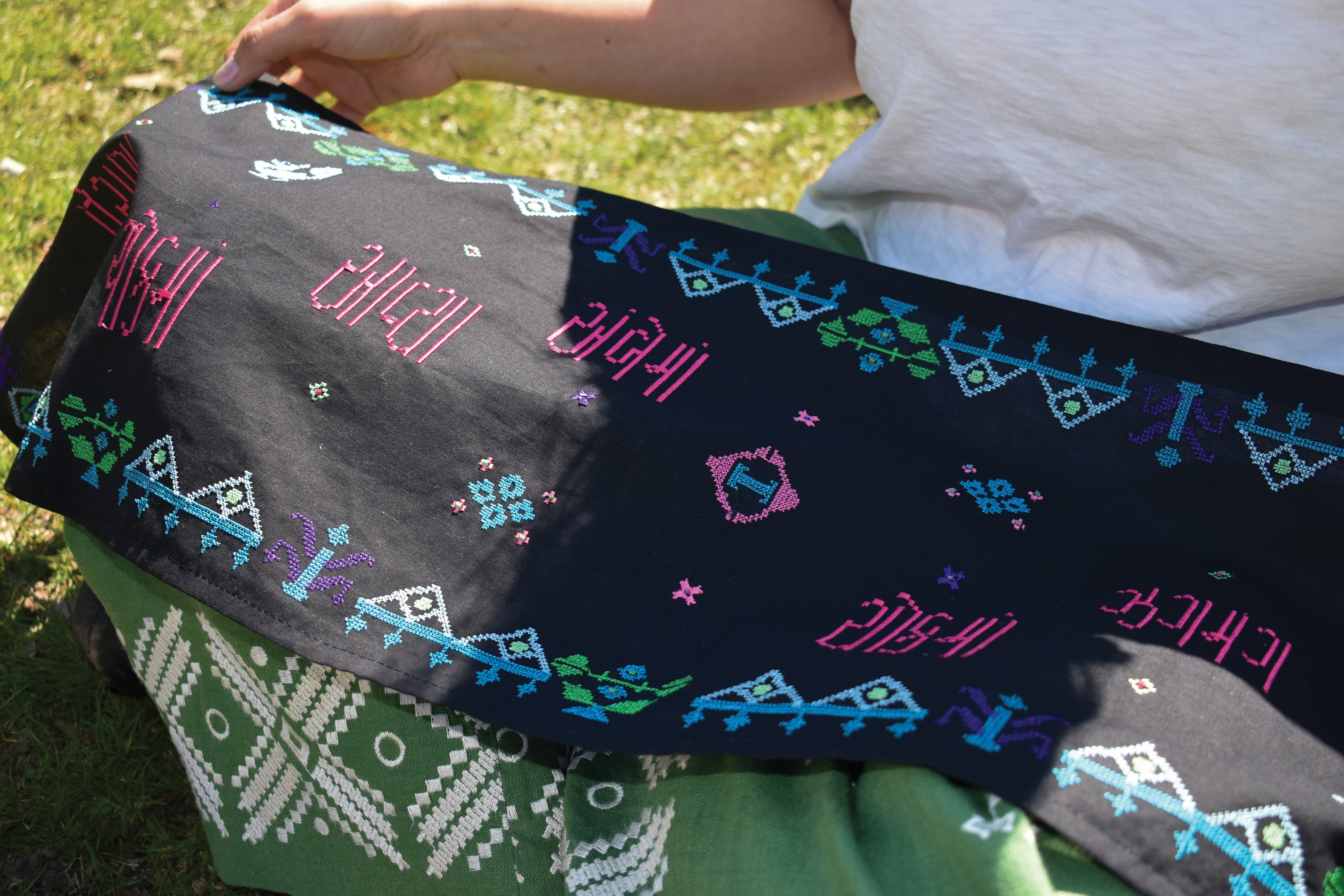 A digitally embroidered scarf displays the Moti typeface in vibrant pink, blue, green, and white threads on dark fabric, featuring Gujarati script and geometric beadwork-inspired motifs scattered across the textile