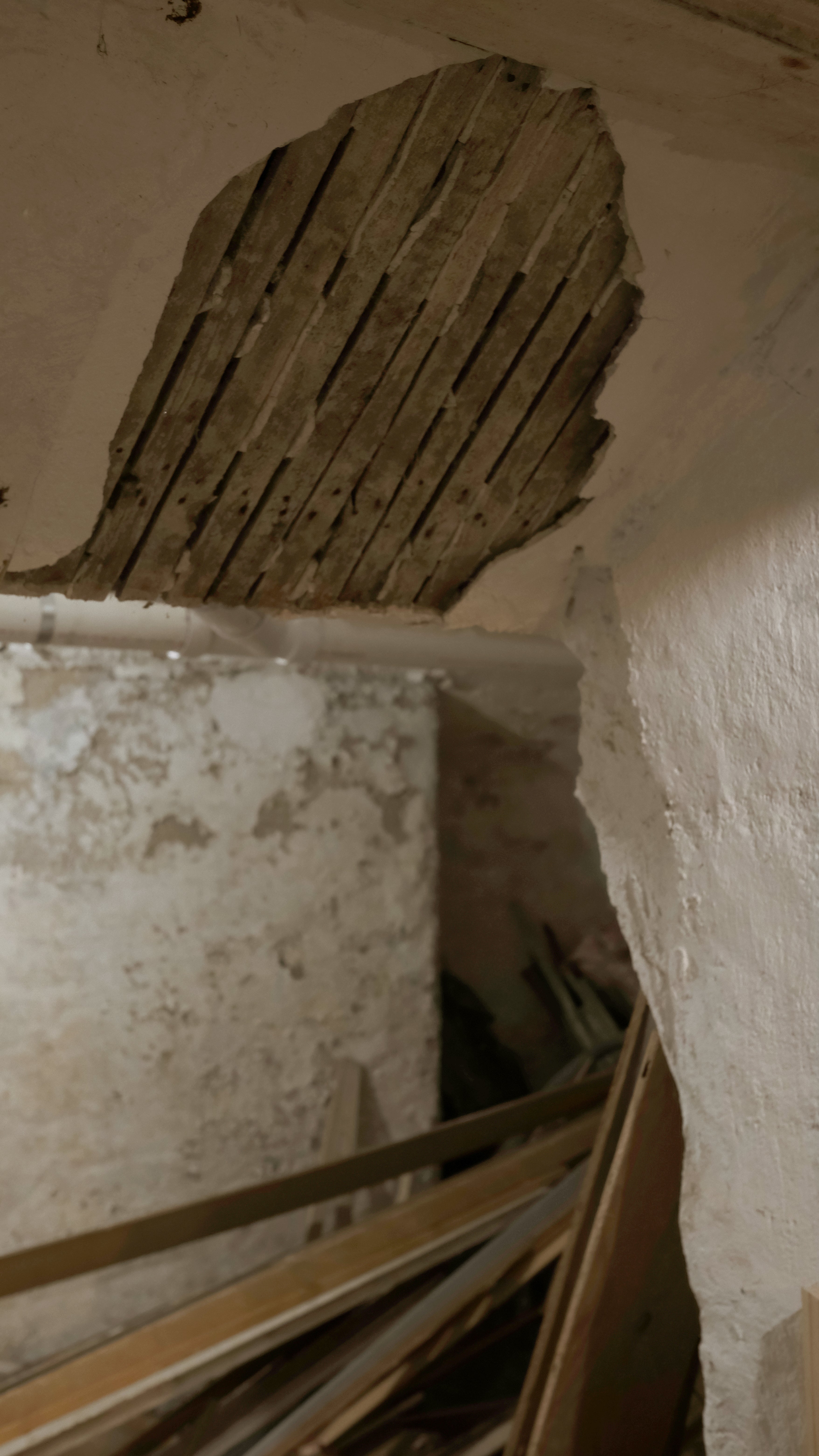 Crumbling plaster on a basement wall revealing wooden lathing beneath, exposing the layered construction of a historic Providence building.