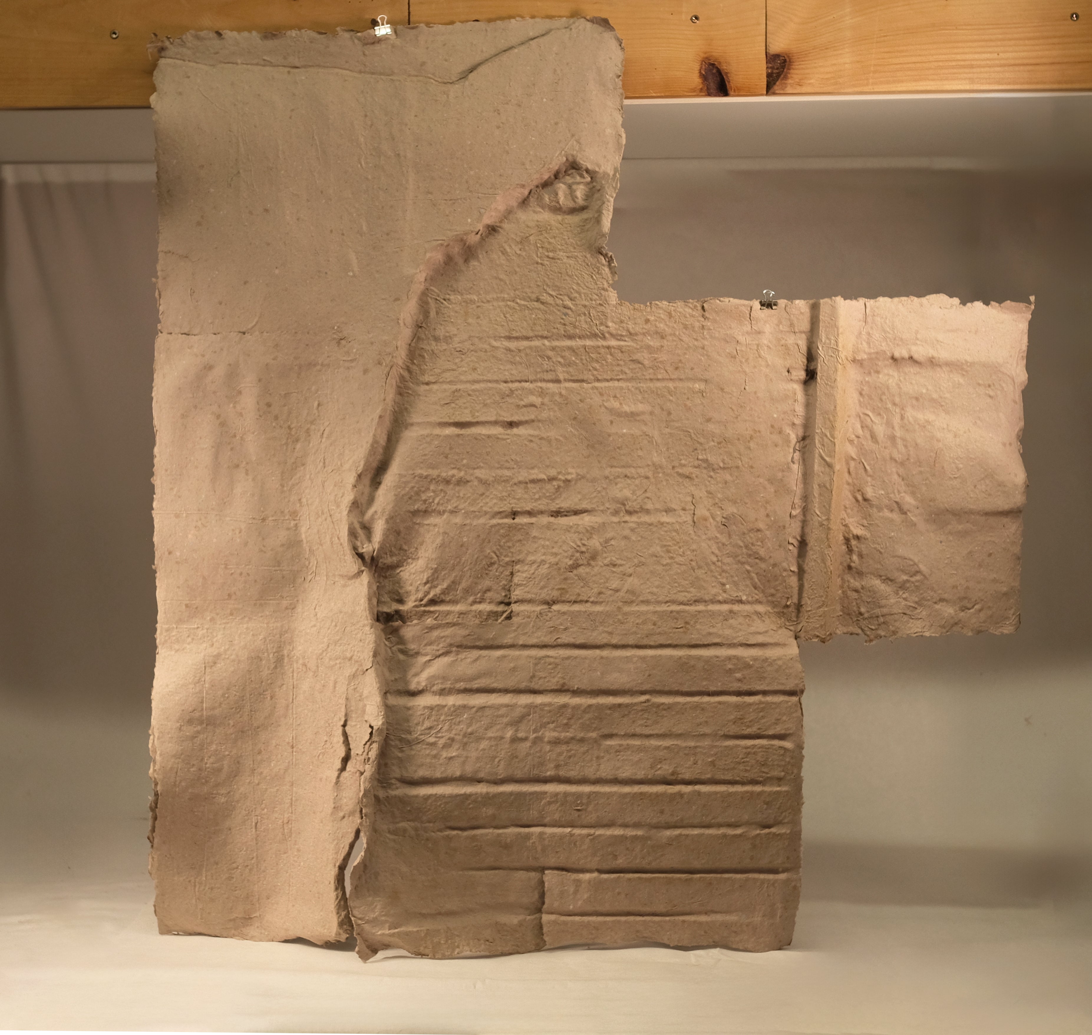 A sheet of handmade paper cast from a basement wall, showing the impressed texture of crumbling plaster, wooden lathing, and brick.