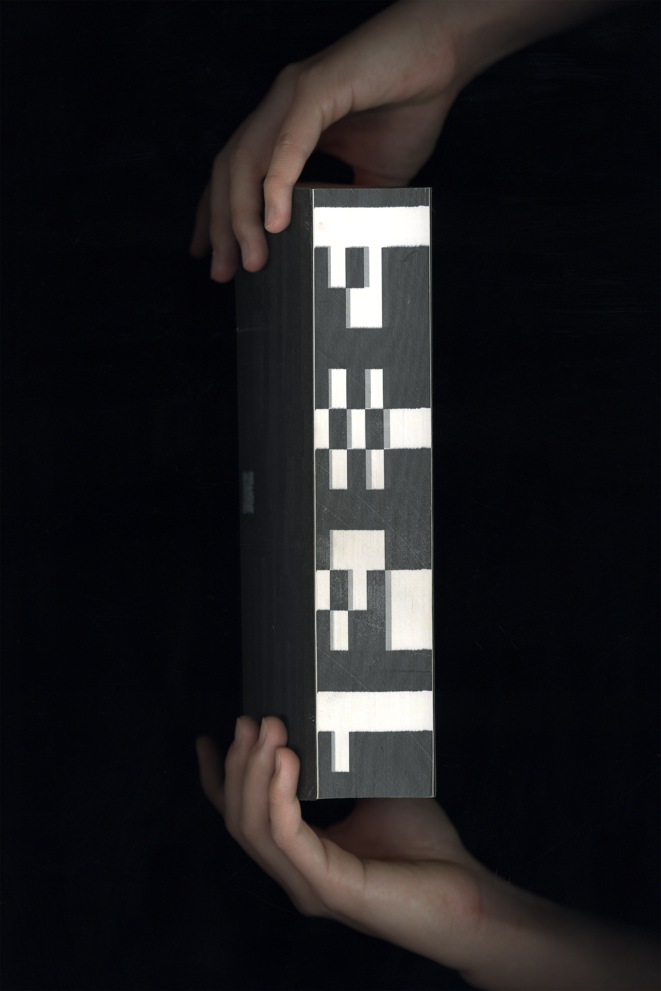 Hand holding a black book titled "1984" on the fore-edge. There is a QR code and an encoded title on the cover of the book.