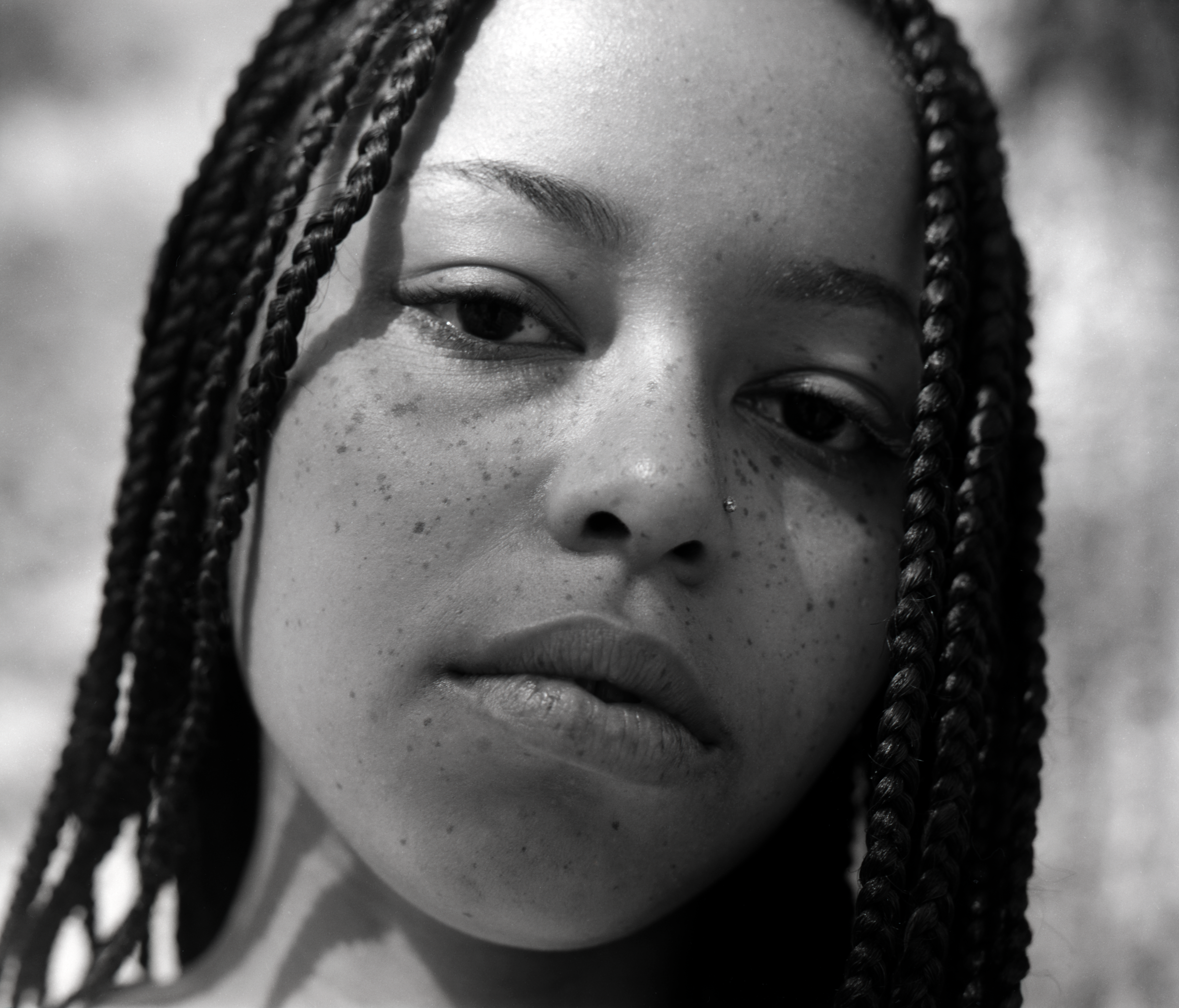 Black and white close-up photograph of a person with braided hair and freckles. Their expression is calm and introspective, conveying a serene and thoughtful mood.