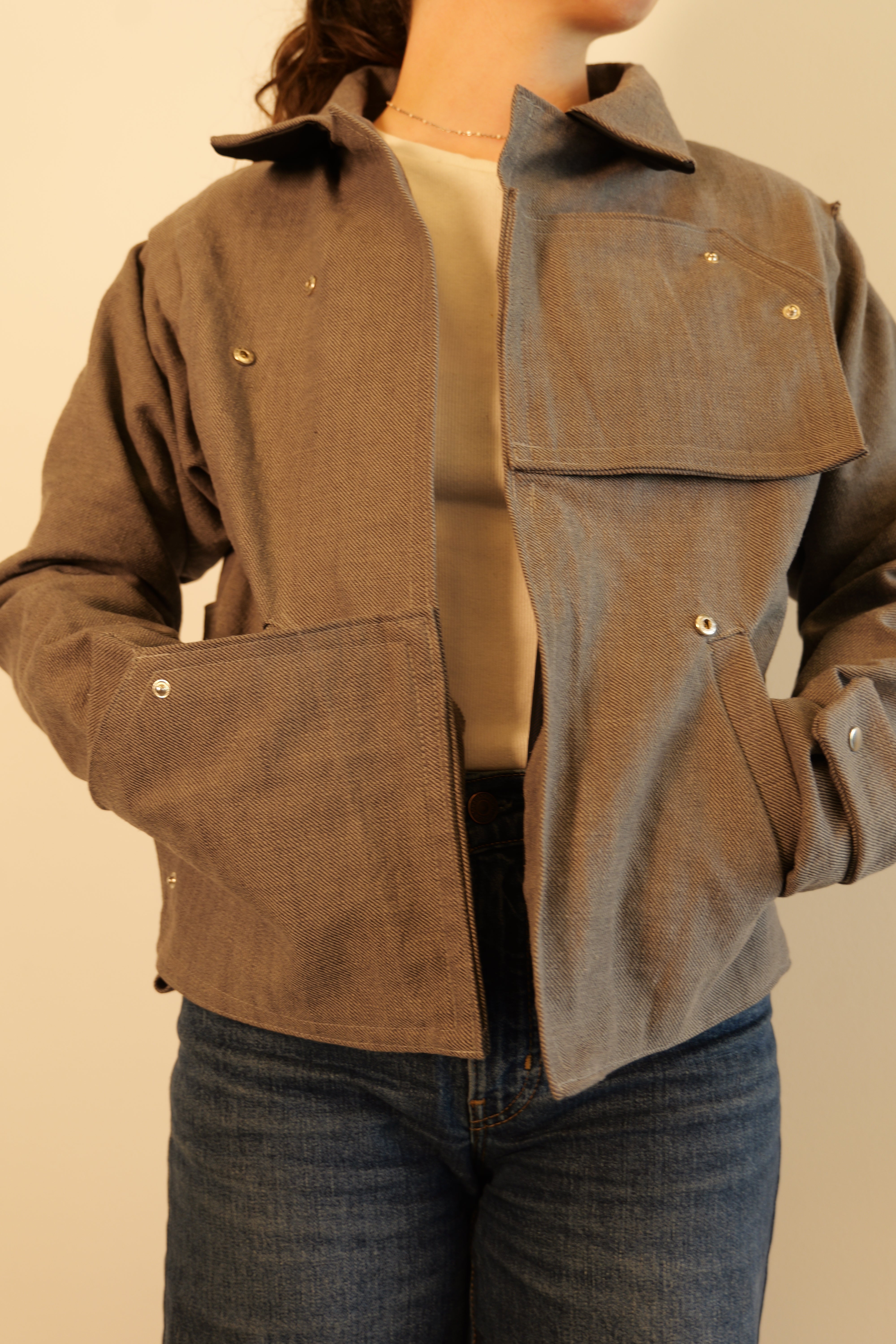 Teammate is wearing a finished grey  jacket made from a repurposed IKEA sofa cover, with silver snap hardware visible across the chest, lower pockets, and cuffs.