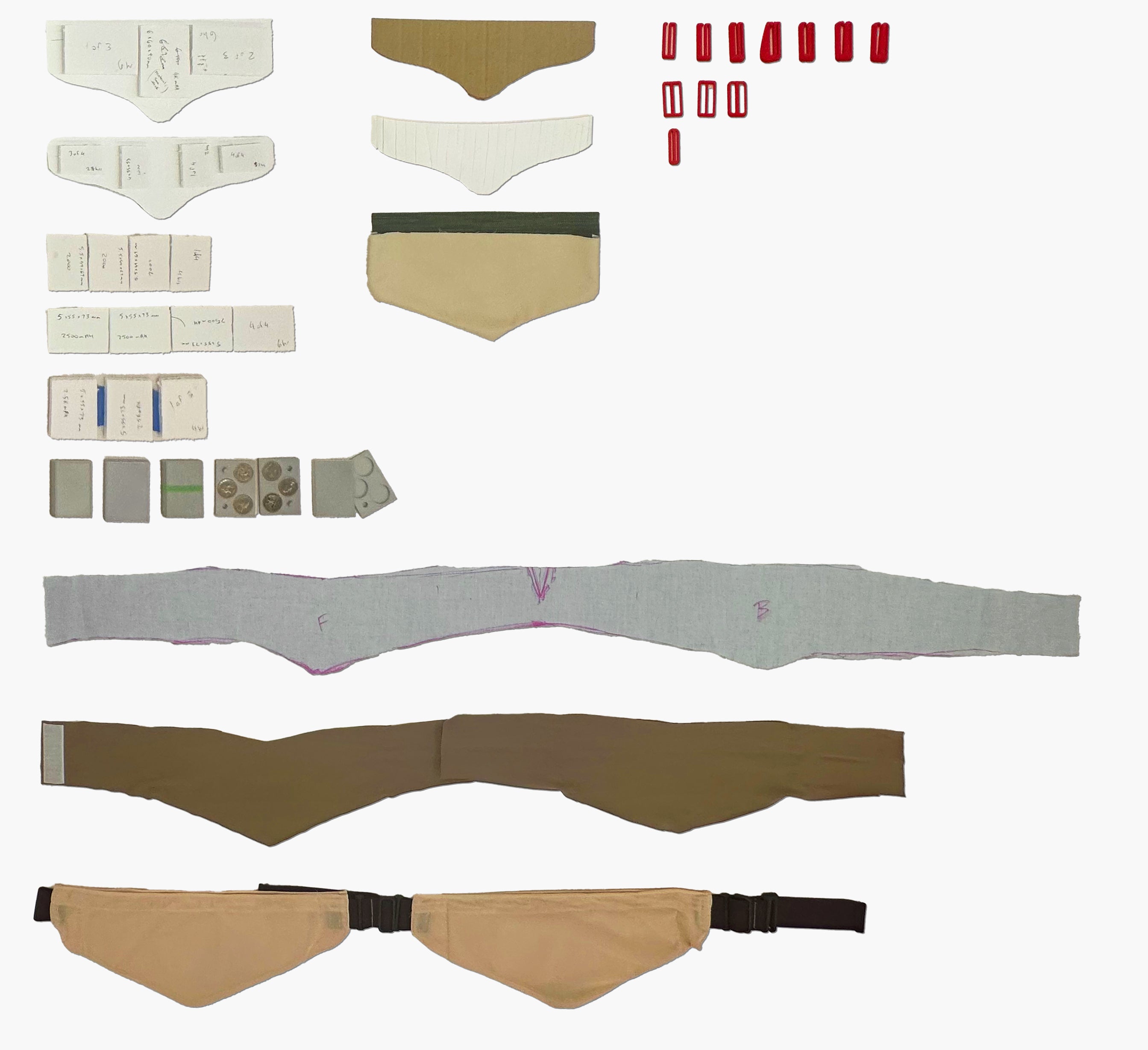 A flatlay of prototypes in process, including clips, fabric belts, and simulated batteries