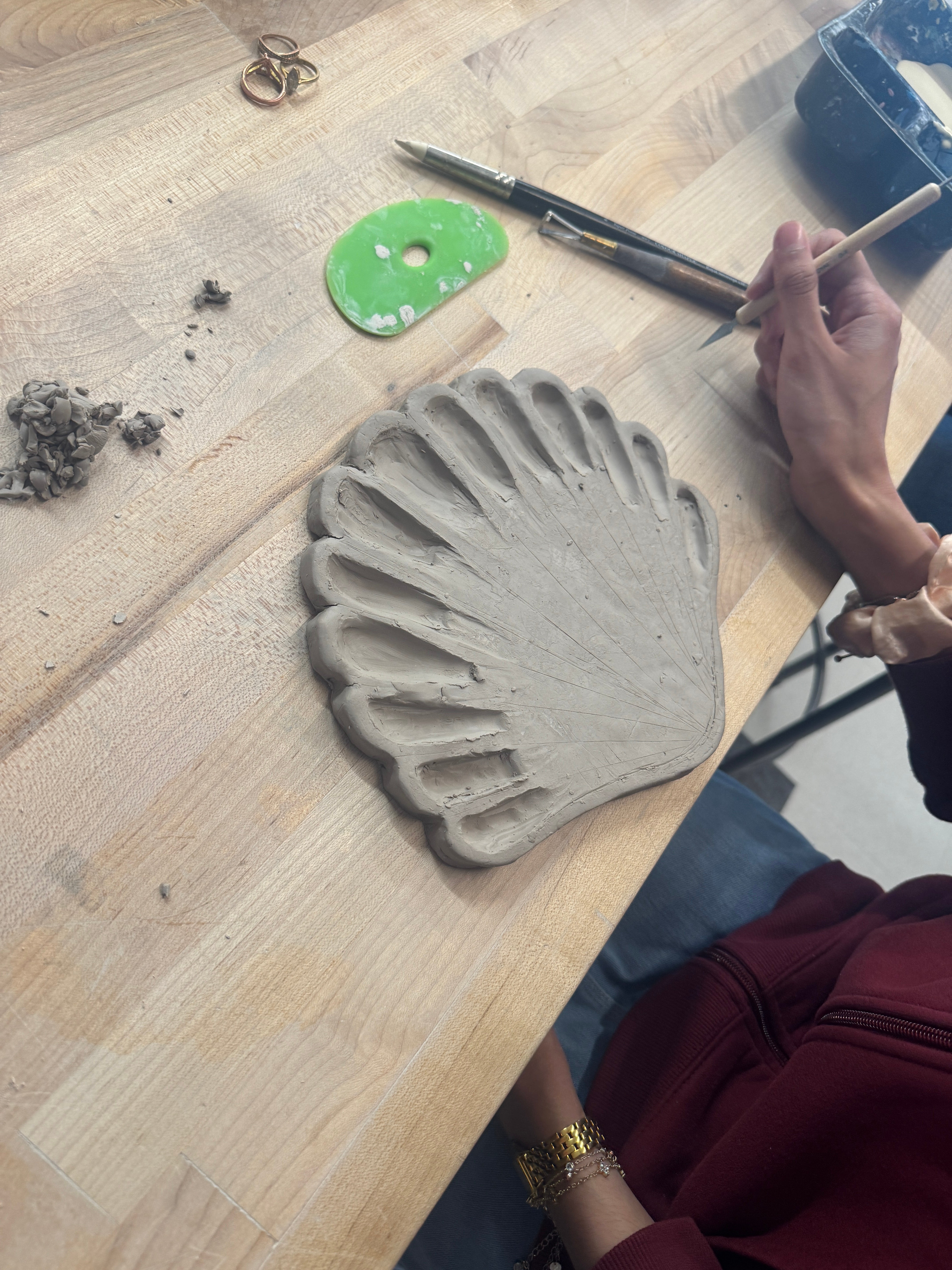 A student out of frame carves a ceramic sea shell into a paint palette