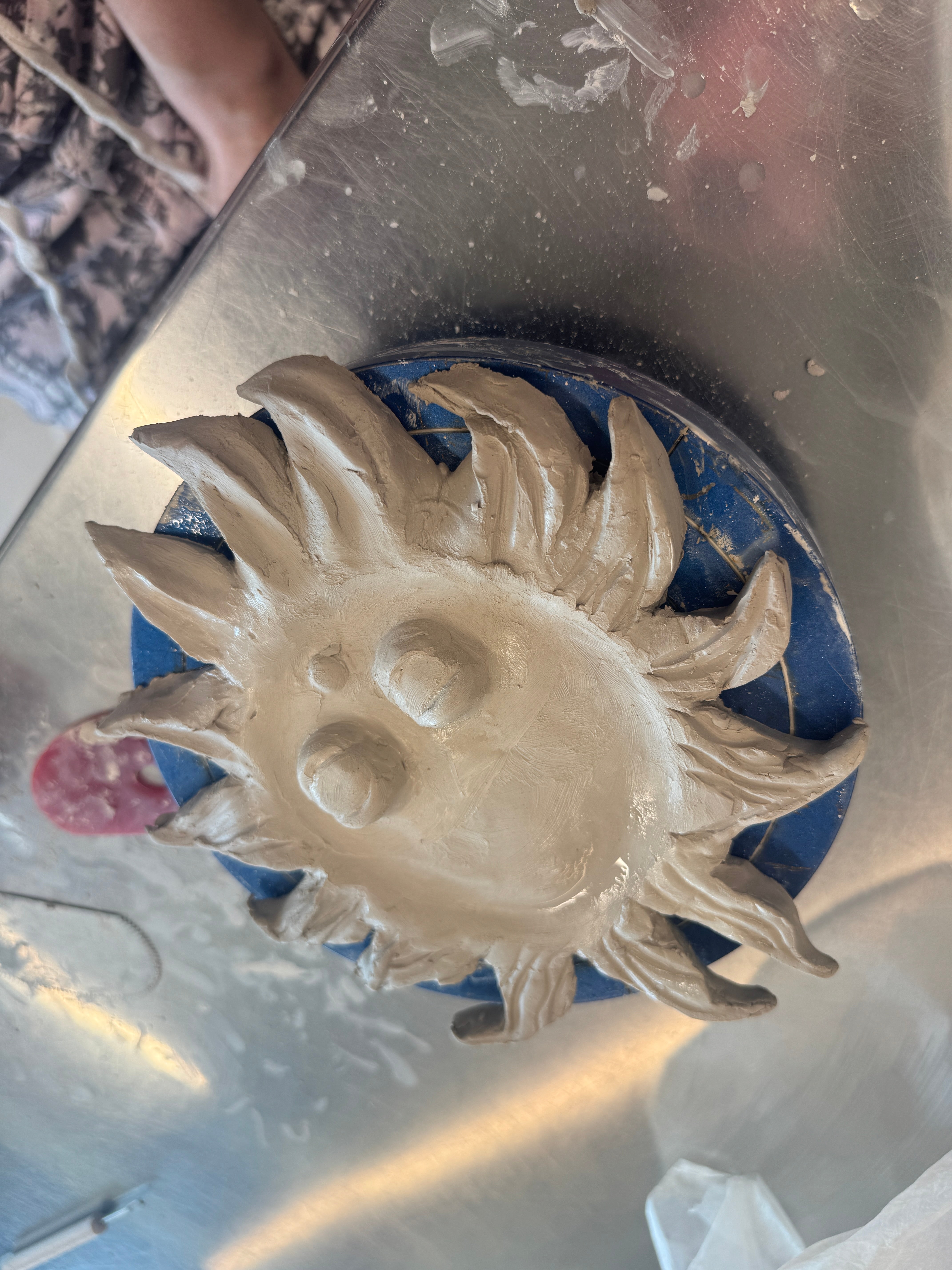 A student out of frame carves an incense holder shaped like a sun with a face