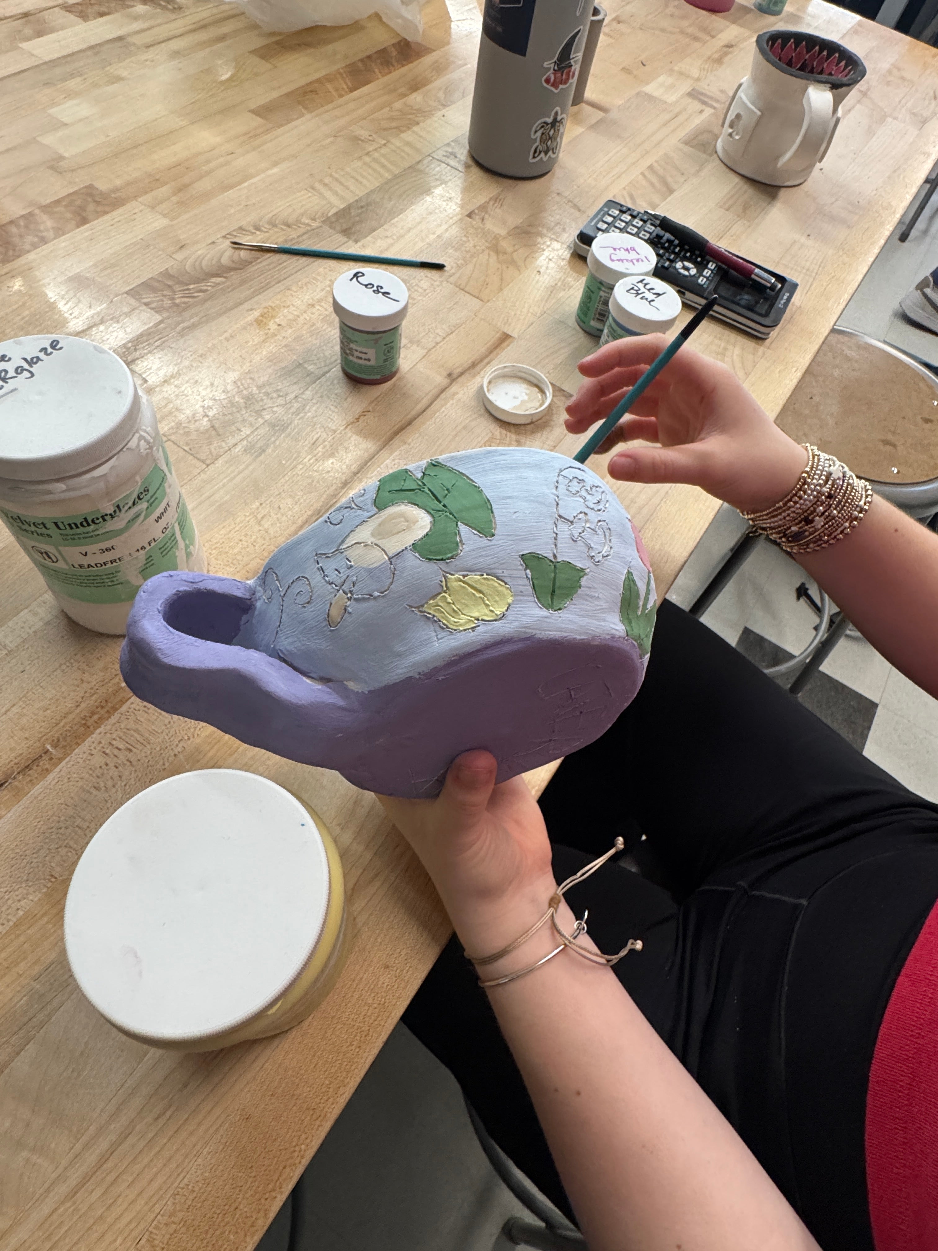 A student out of frame glazes an oversized tea cup with flowers on a blue and purple background