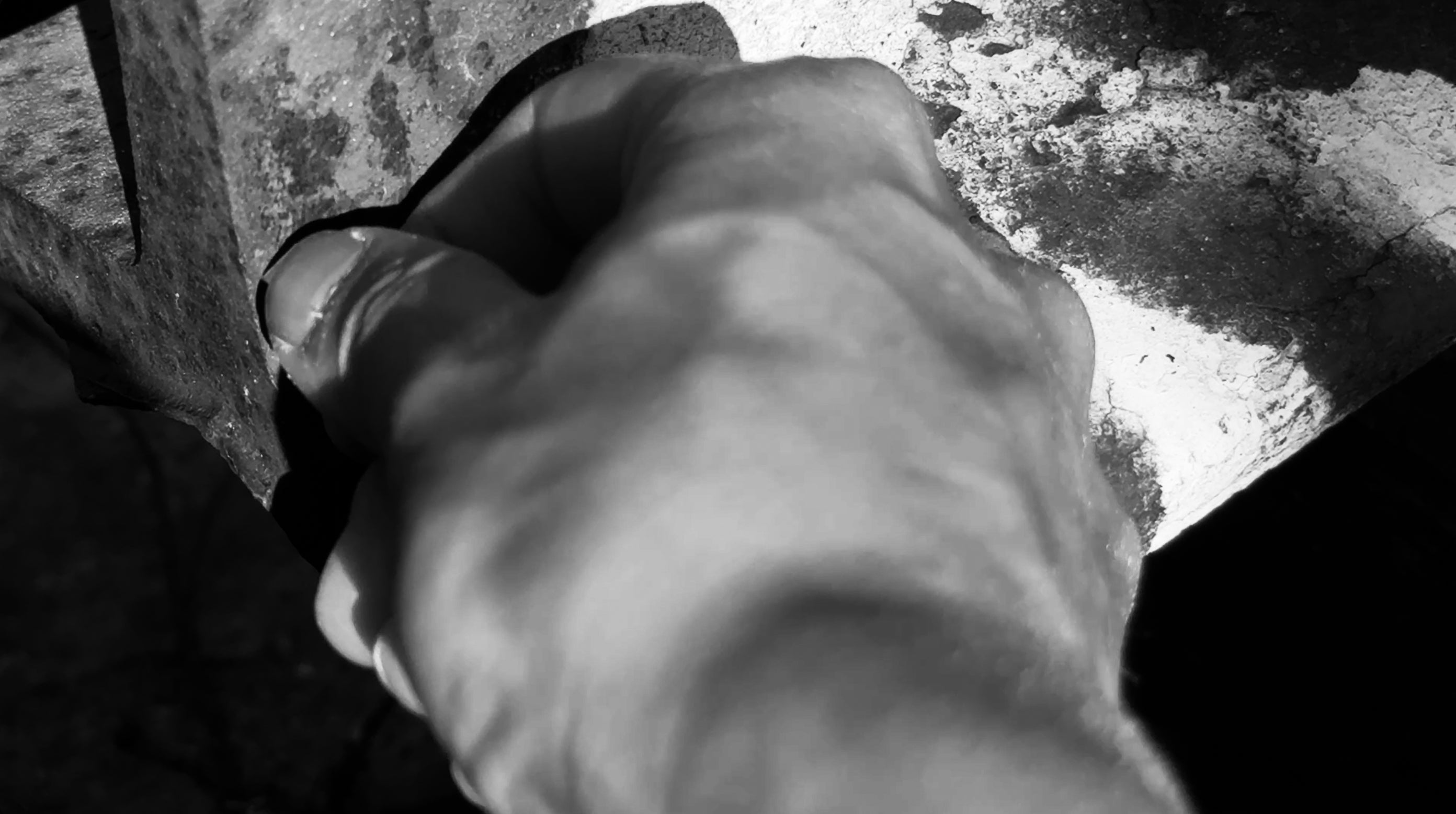 A close-up black and white shot with a hand scratching on the rusty metal surface with white graffiti.