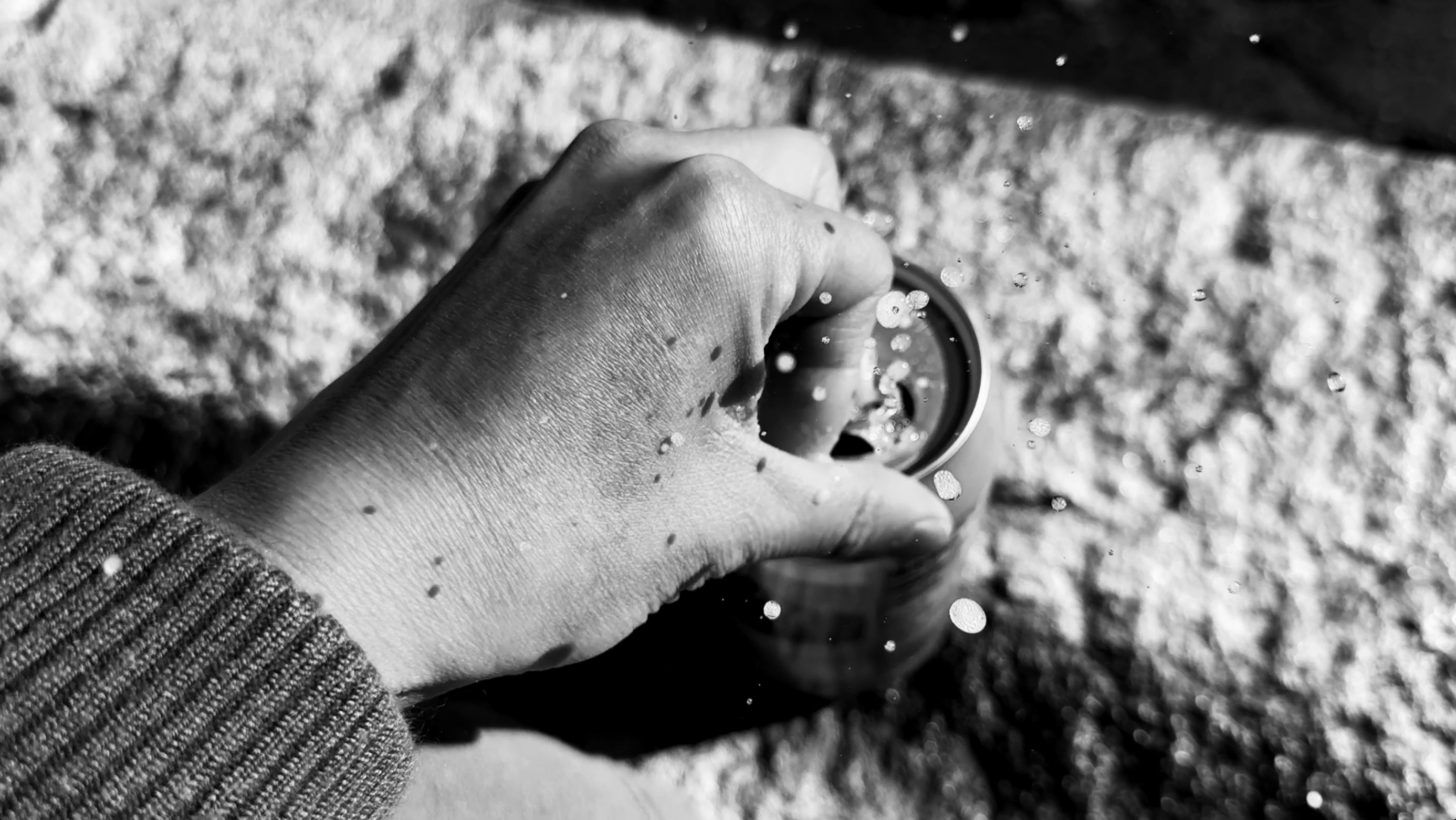 A black-white close-up photo of a hand opening a sparkling water with the liquid splashing out.