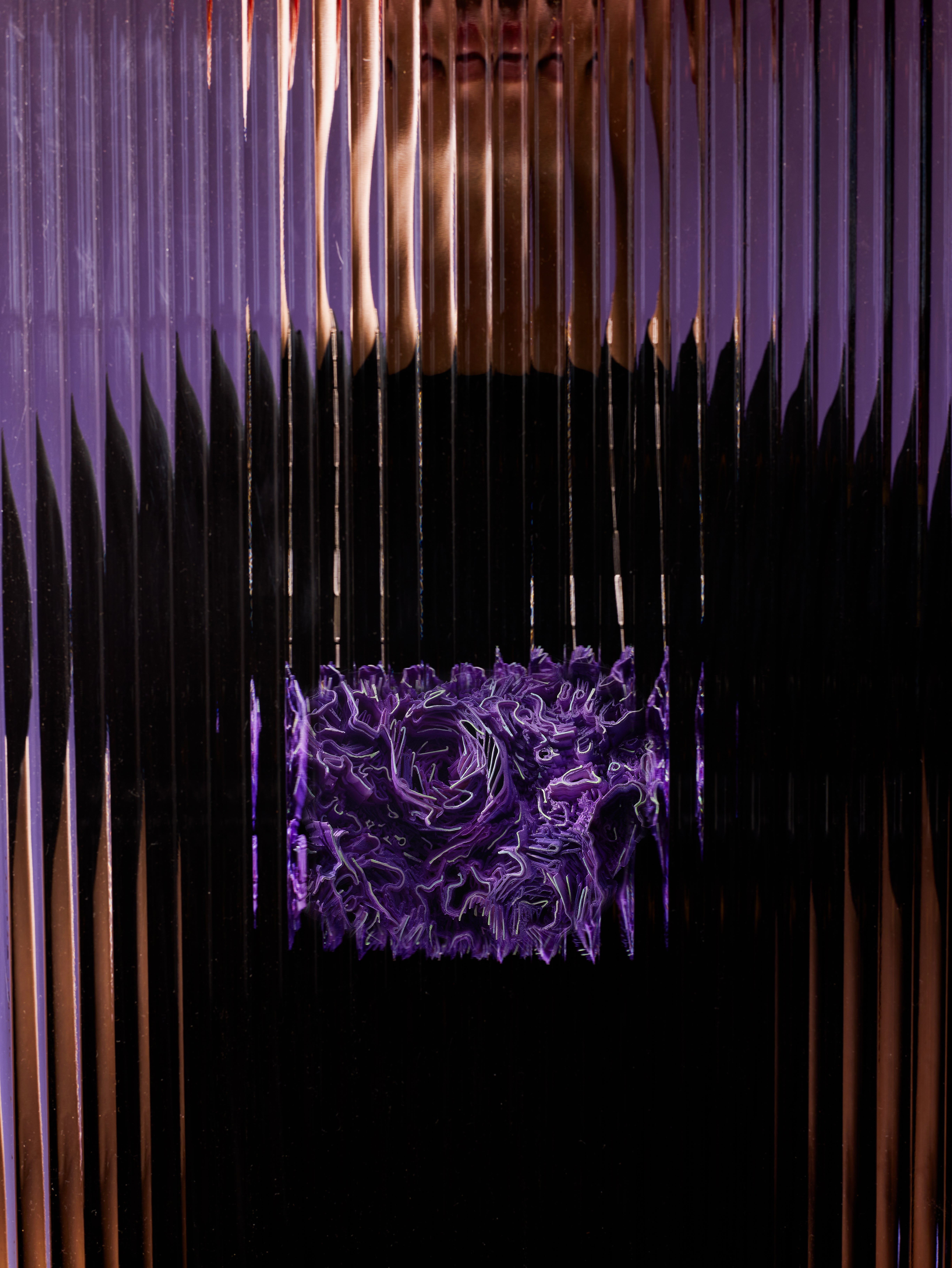 Curved purple necklace with a dense surface of small wall-like forms rising and falling, hanging from a thin silver chain.
