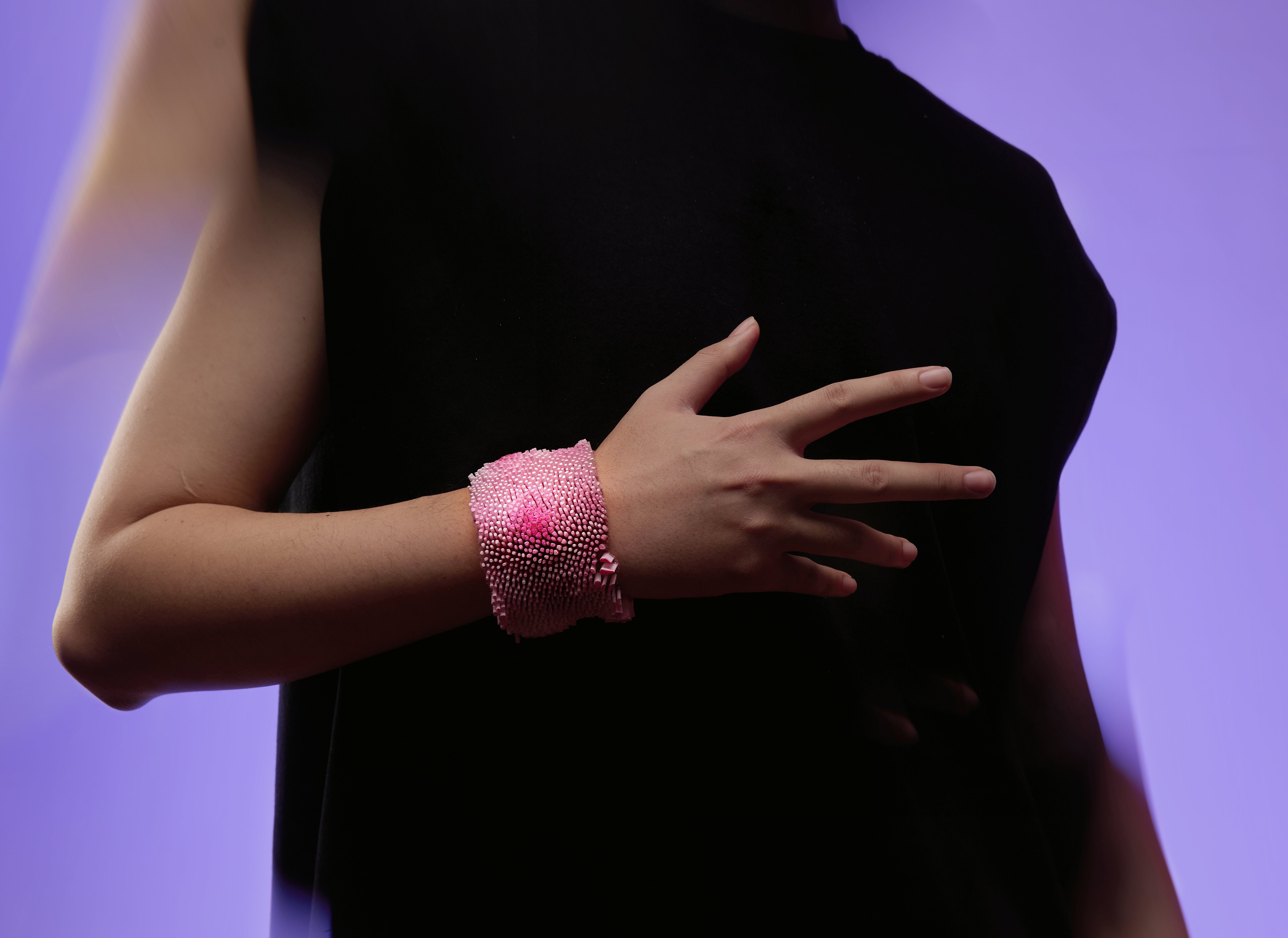 Pink bracelet covered in densely packed small upright elements on mesh, with darker pink areas creating depth variation.